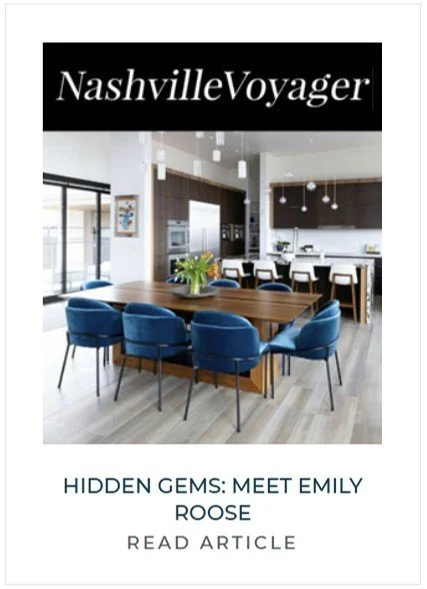 Modern kitchen with a dining area, featuring a wooden table surrounded by blue chairs, in a bright space with large windows and pendant lighting.