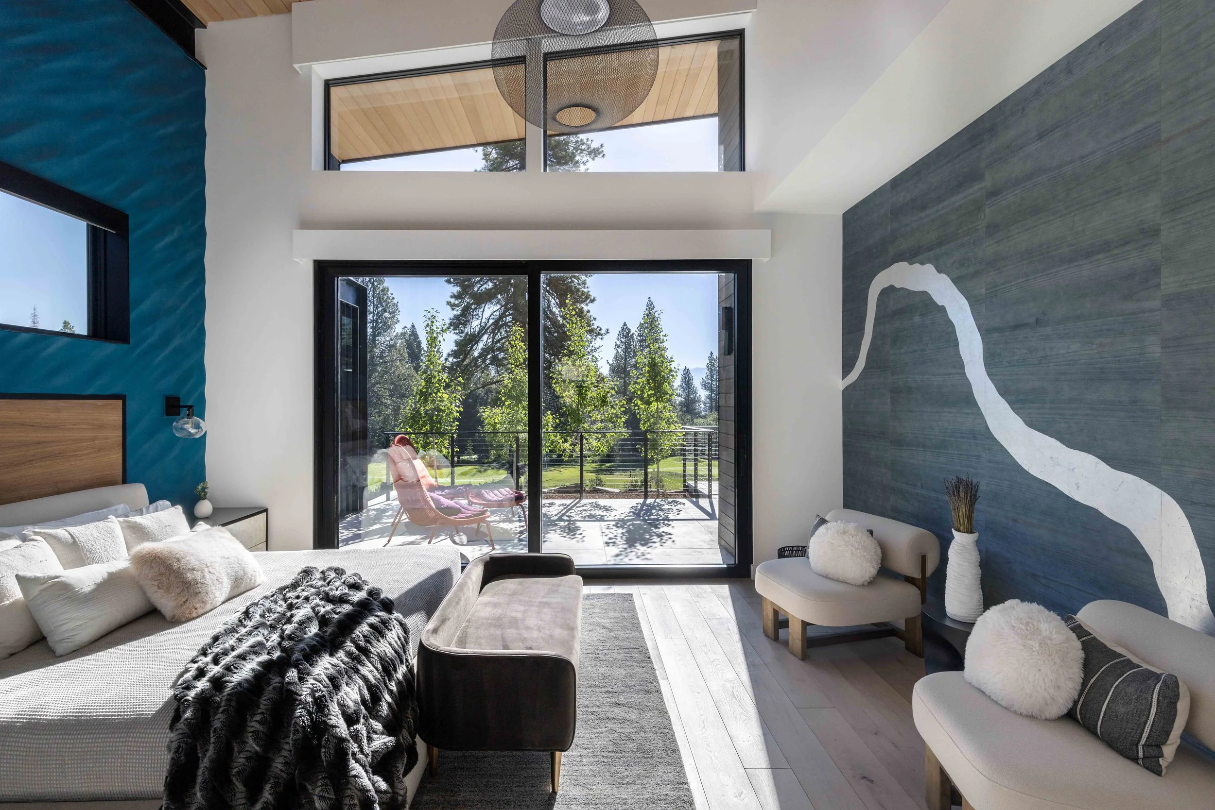 Modern living room with large glass sliding door leading to a balcony with outdoor seating, detailed blue and white walls, and a view of trees outside.