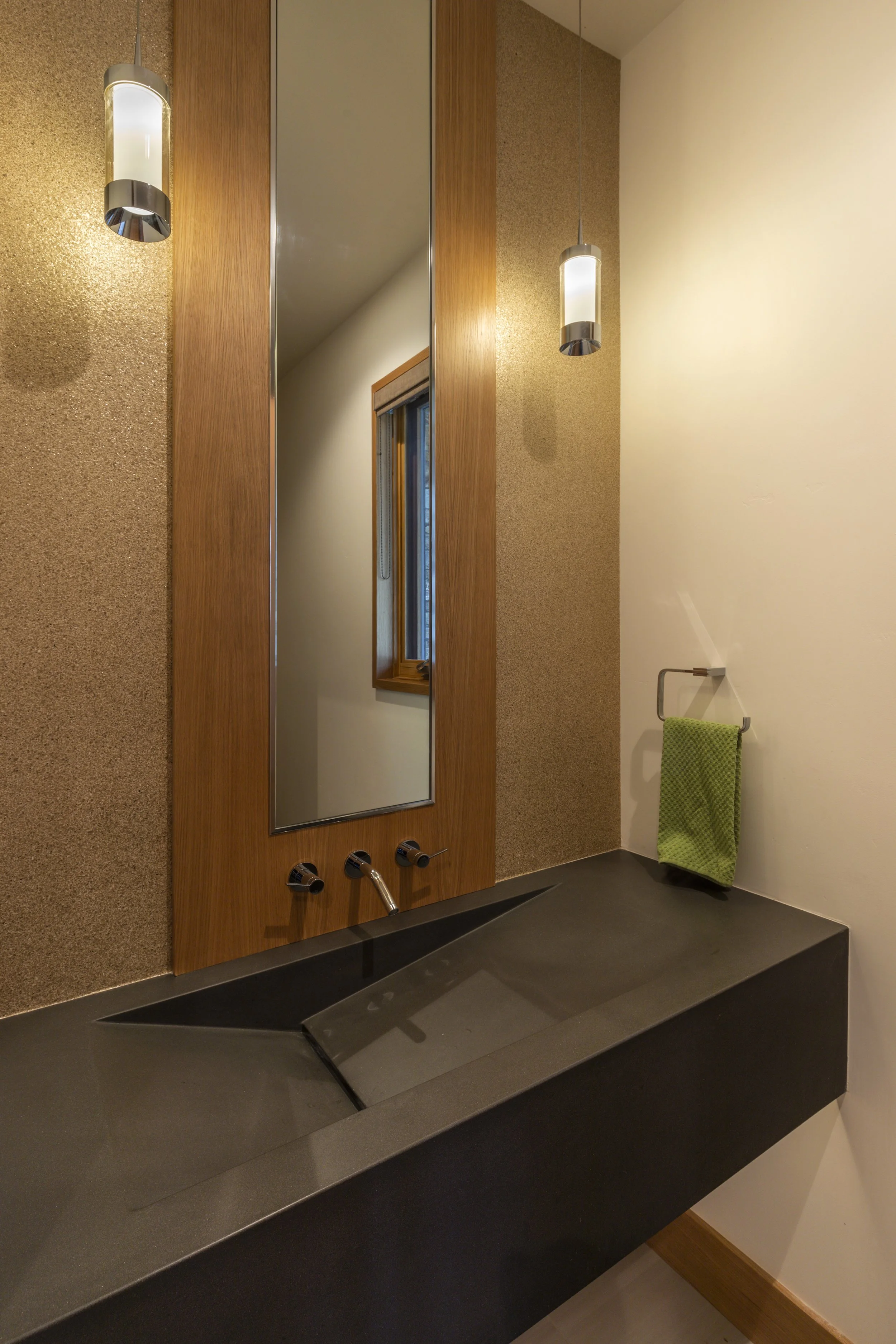 Modern bathroom with a black sink, a wood-framed mirror, pendant lights, a towel holder with a green towel, and a window.