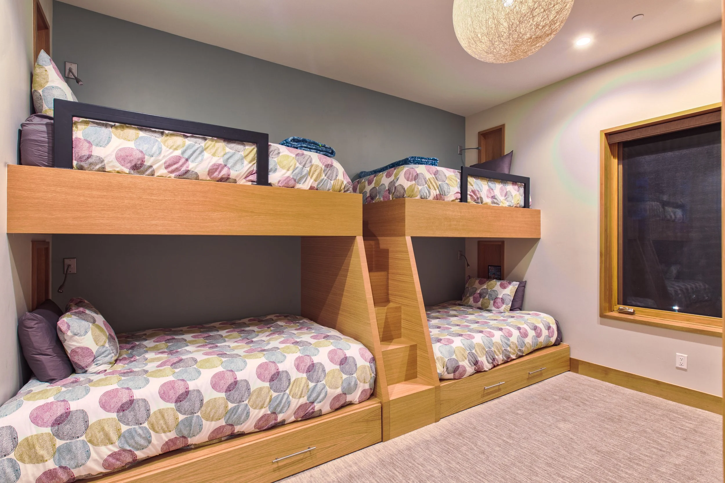 Bedroom with two sets of bunk beds made of wood with polka dot bedding, pillows, and a window with wooden trim.