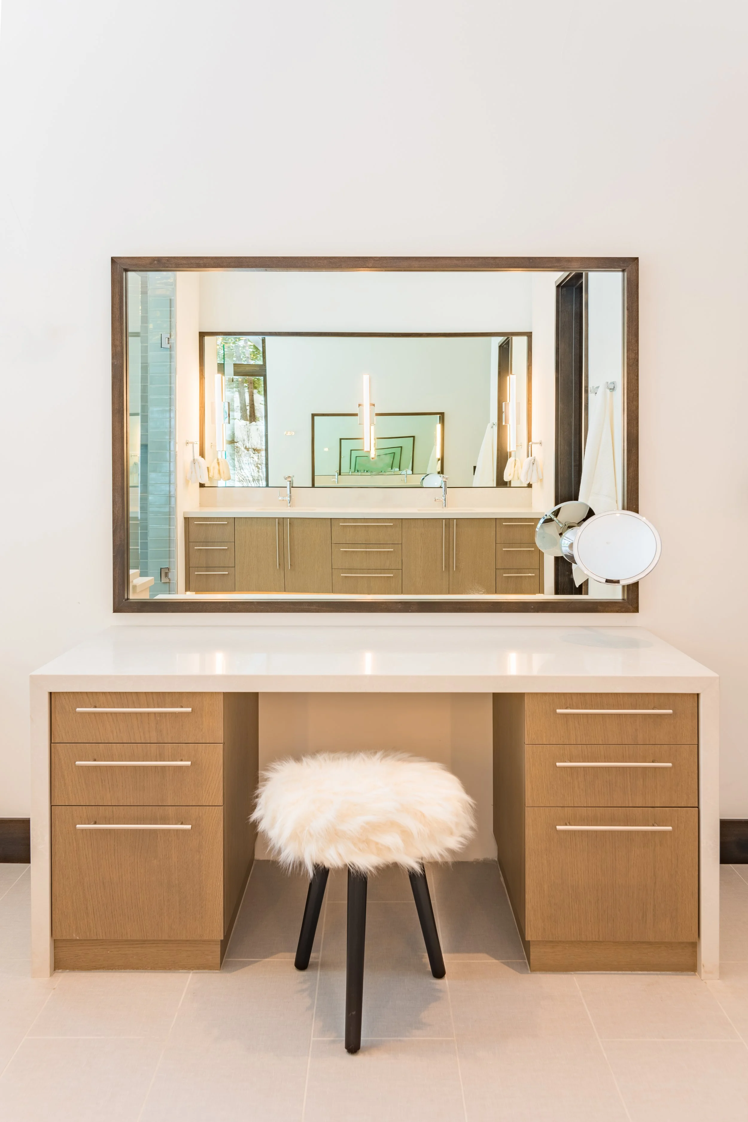 Bathroom vanity with large mirror, wooden cabinet, makeup mirror, and furry stool.