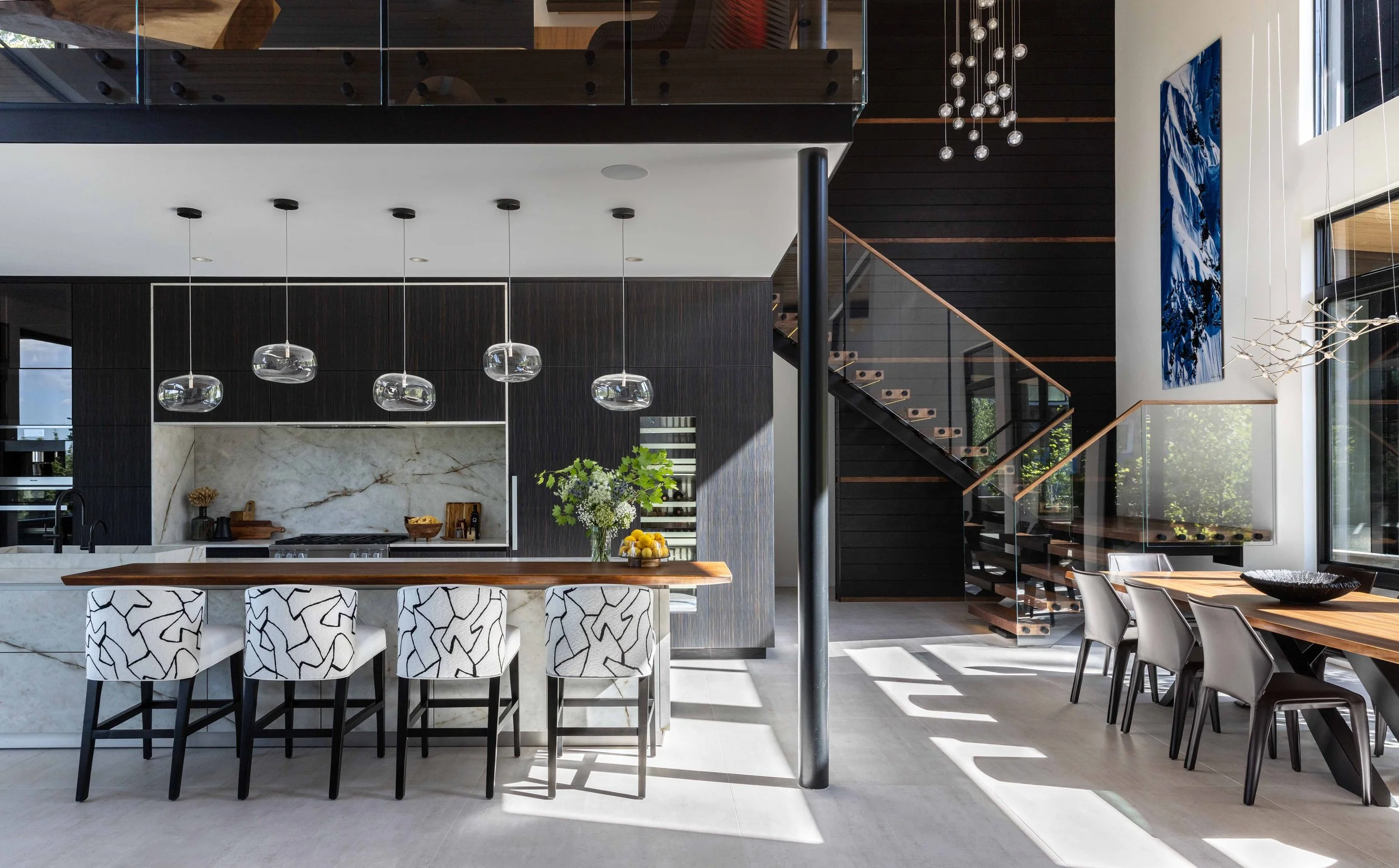 Organic Mountain Modern kitchen with Himalaya Crystal porcelain countertops and backsplash with a live edge walnut counter suspended on the island, black and brown cabinets mixed with porcelain cabinets, glass pendant lights, and a wood staircase.