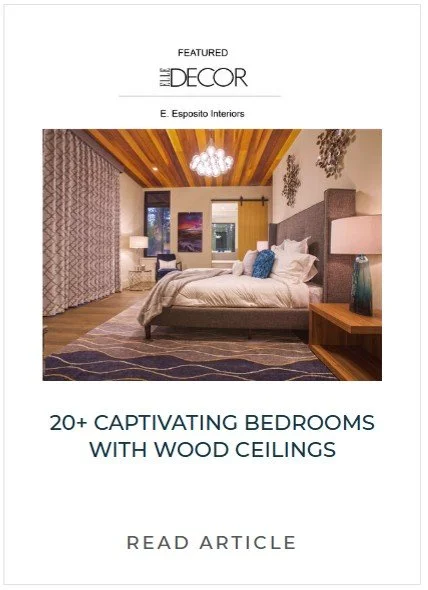 A bedroom with wood ceiling, large bed with white and blue bedding, nightstand with lamp, curtains, and decorative wall art.