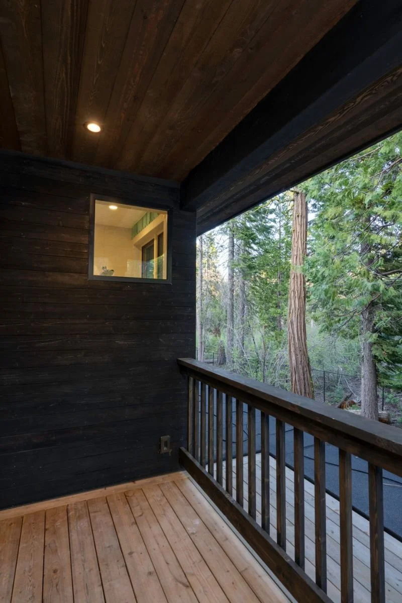 View of a wooden balcony with railing, overlooking a forest of tall trees.