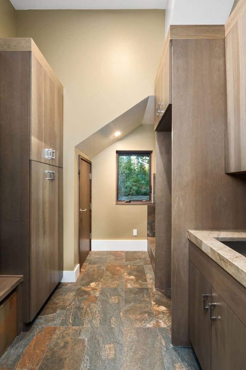 Kitchen with natural wood cabinets, a small window showing trees outside, and multi-colored stone tile flooring.