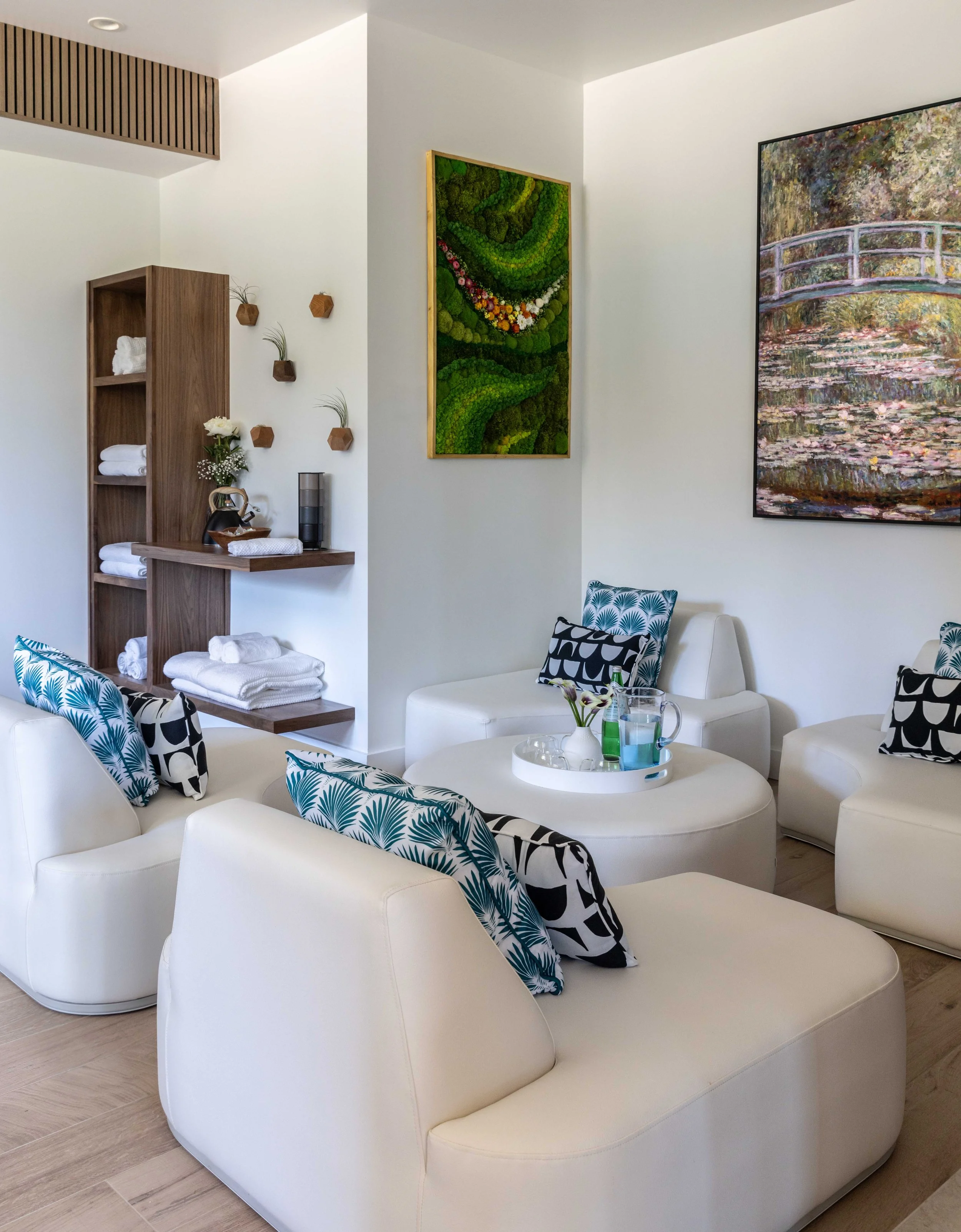 Modern living room with white furniture, decorative pillows, wall art, and a wooden shelving unit.