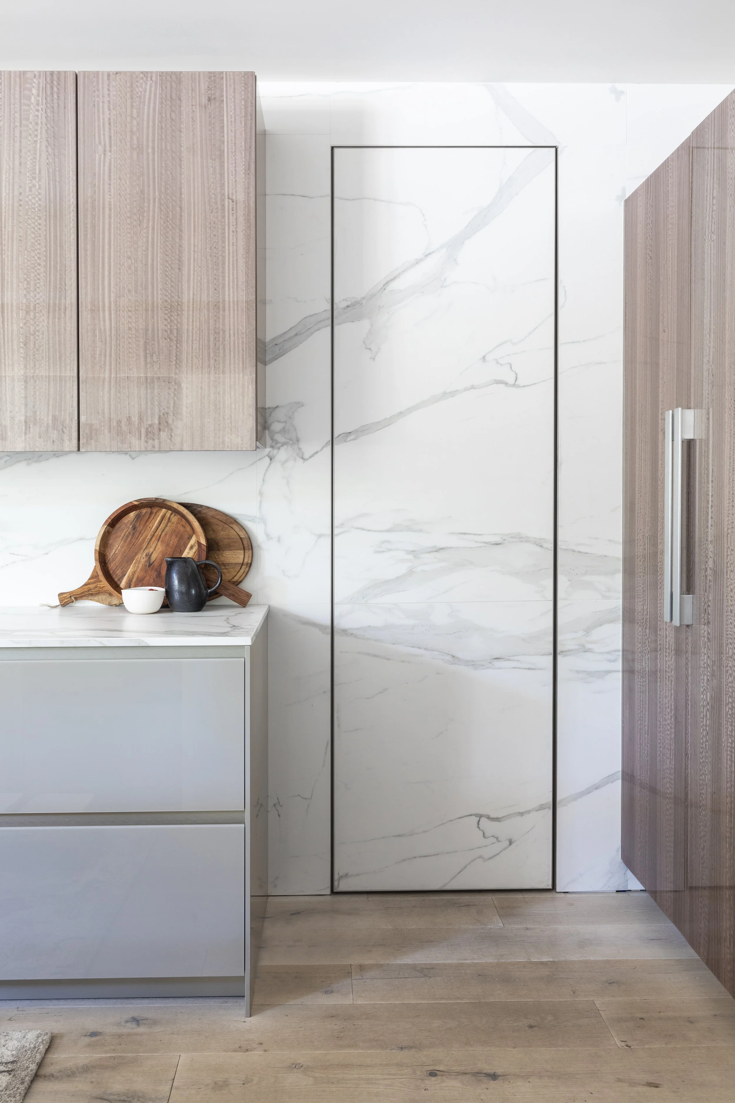 Mountain modern kitchen with porcelain countertops and backsplash in Martis Camp Truckee CA. Cabinets are a taupe glass and resin coated eucalyptus. Hidden pantry door.