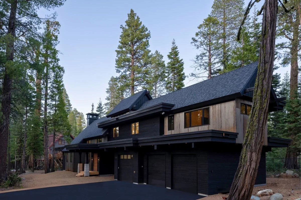 Modern black house with large windows, set among tall trees in a forest.
