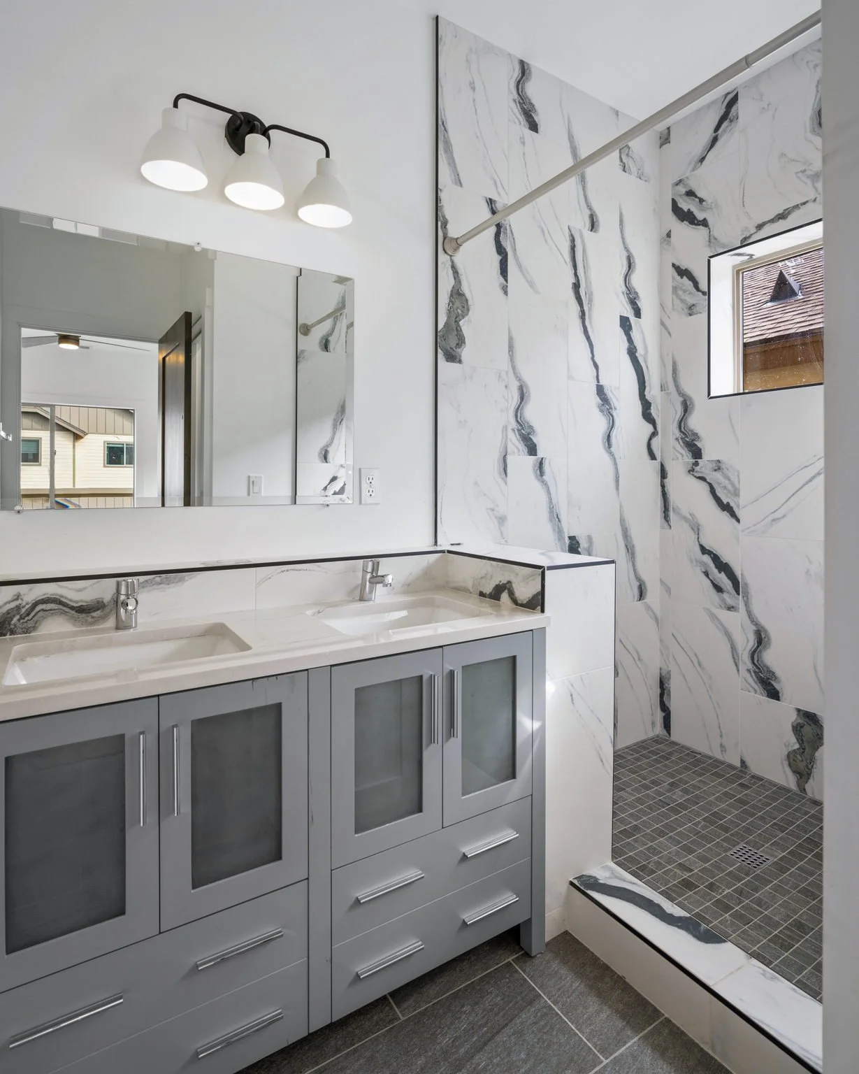 A modern bathroom with a double vanity mirror, a marble backsplash, and a walk-in shower with marble walls and a small window.
