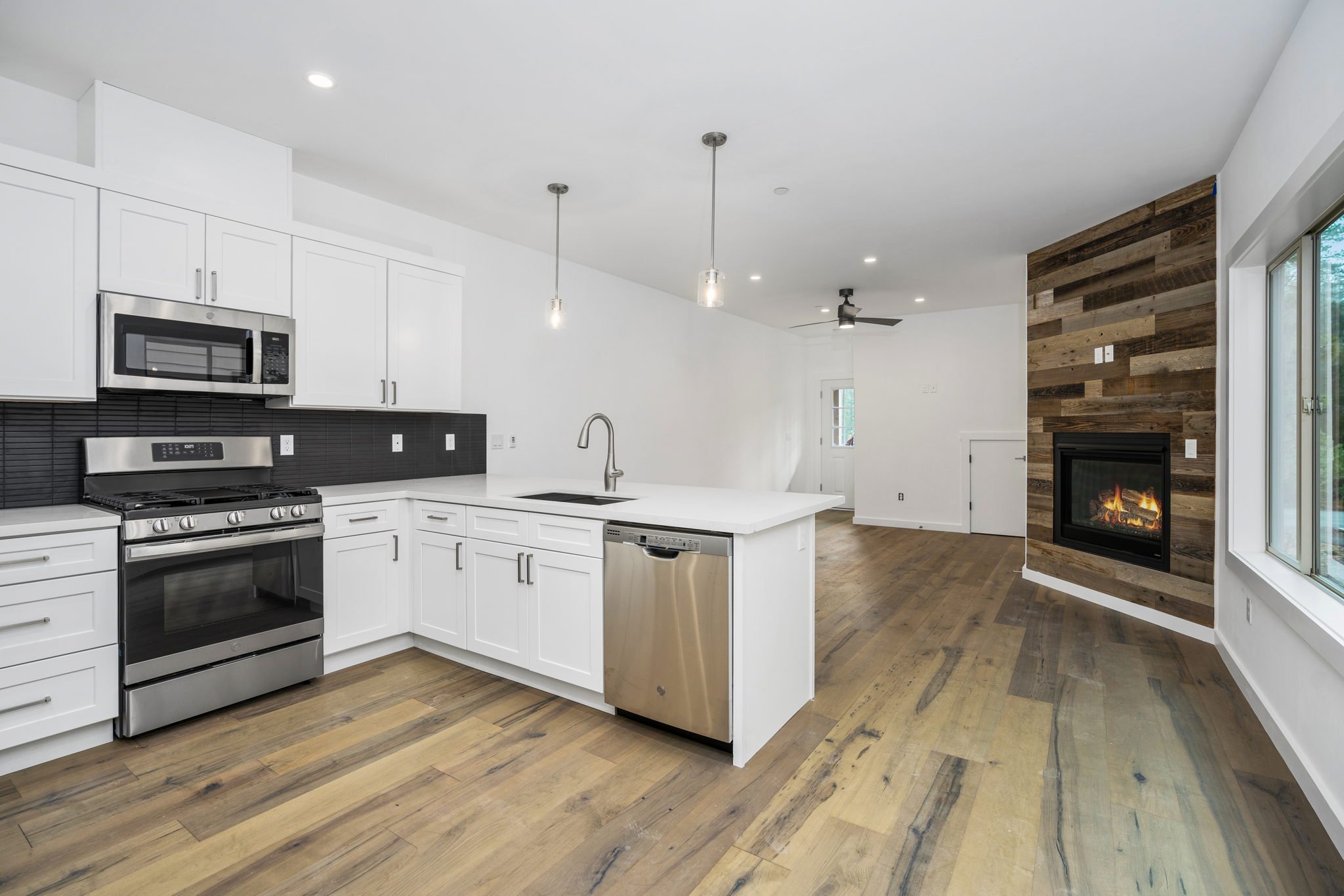 Modern kitchen with white cabinets, black backsplash, stainless steel appliances, and a wood-paneled fireplace