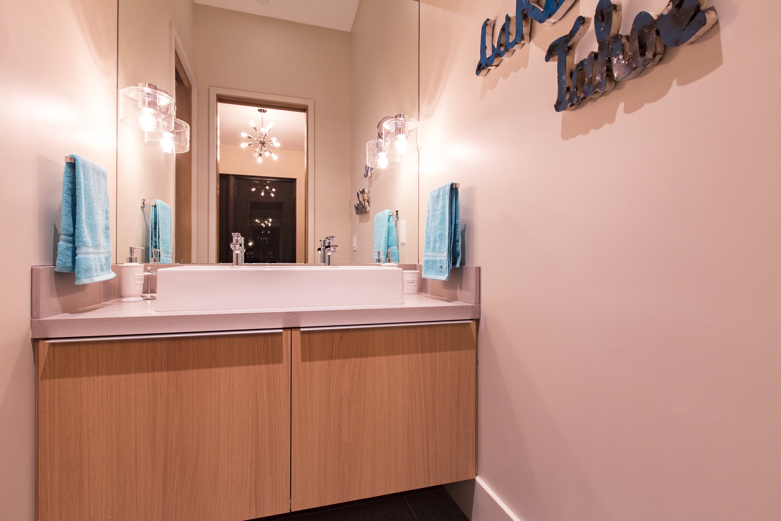 Bathroom with double sink vanity, light blue towels, large mirror, wall decor, and modern lighting fixtures.