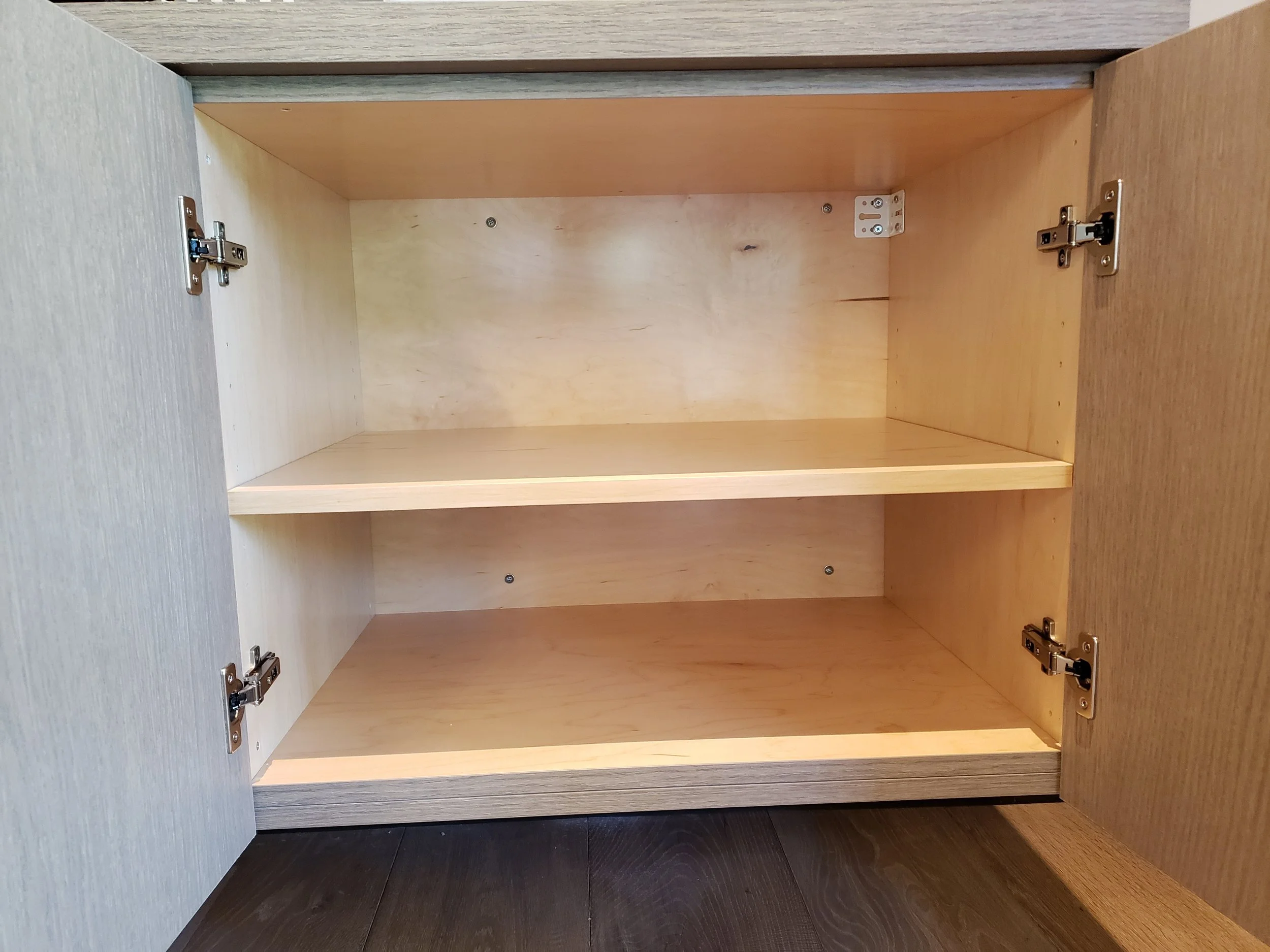 Empty wooden cabinet with two shelves inside and metal hinges on the doors.