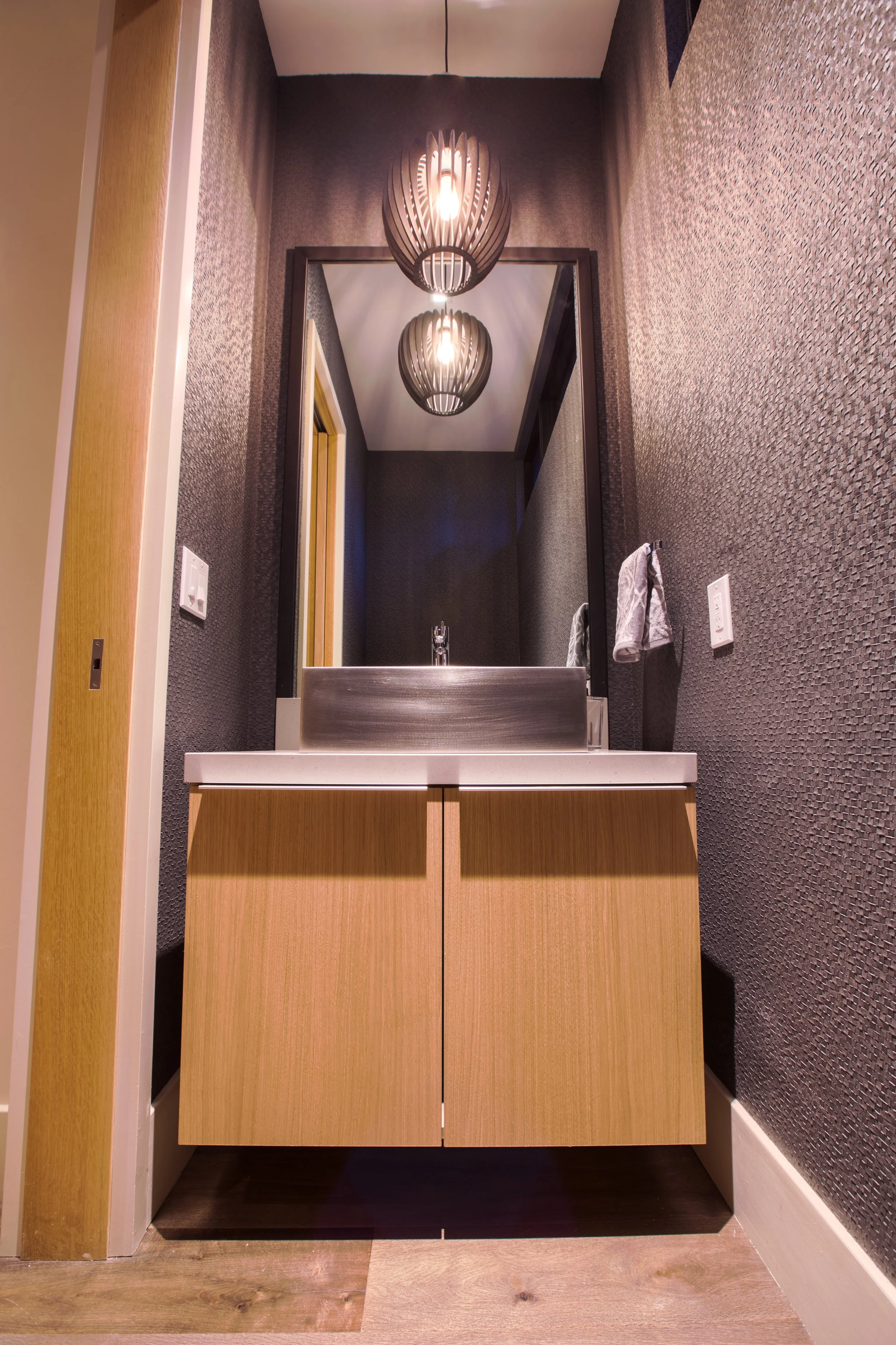 Modern bathroom vanity with a mirror, two pendant lights, and textured dark wallpaper.