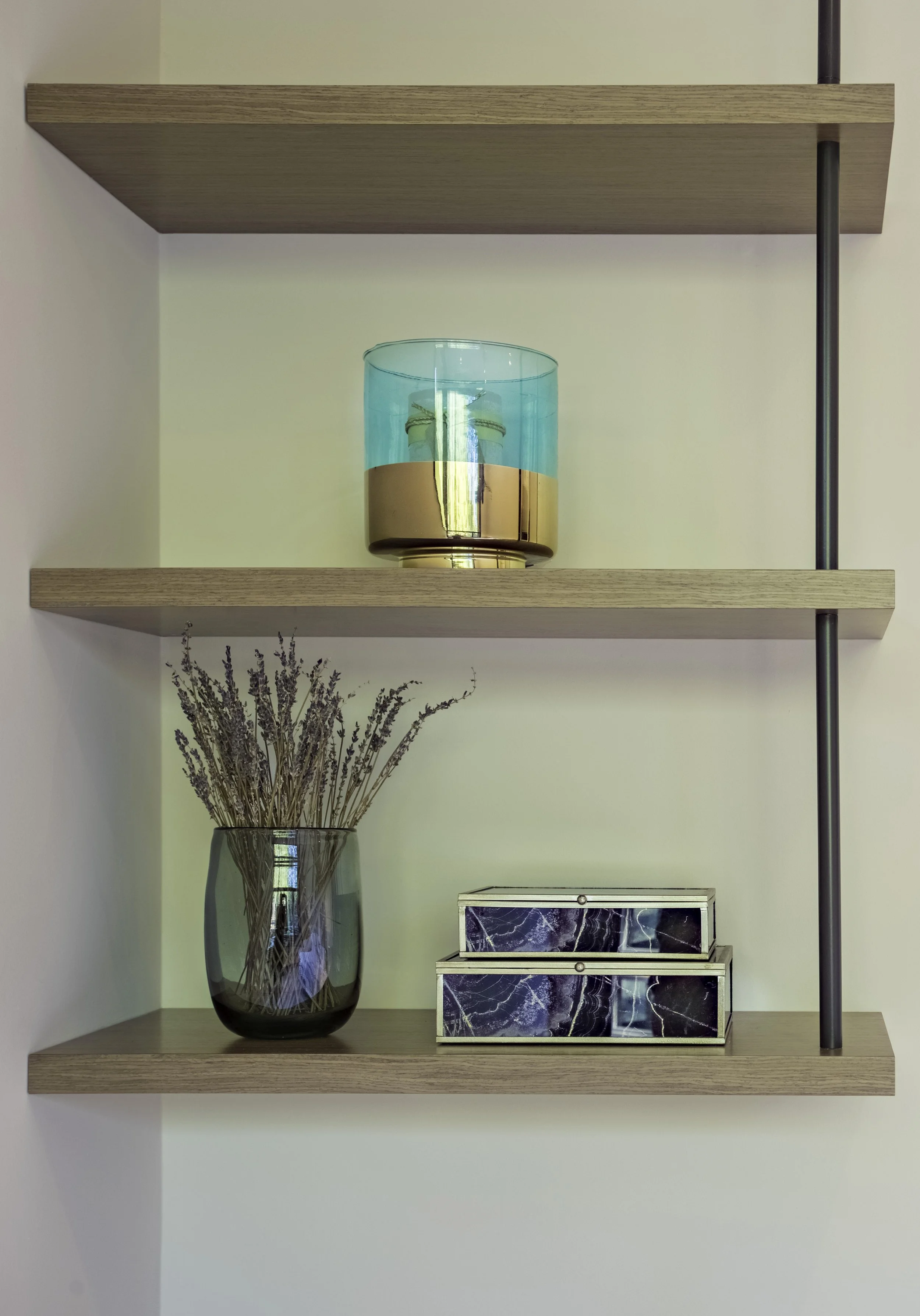 Wall-mounted wooden shelves holding a blue and gold decorative glass, a black vase with dried lavender, and two mirrored boxes with marble designs.