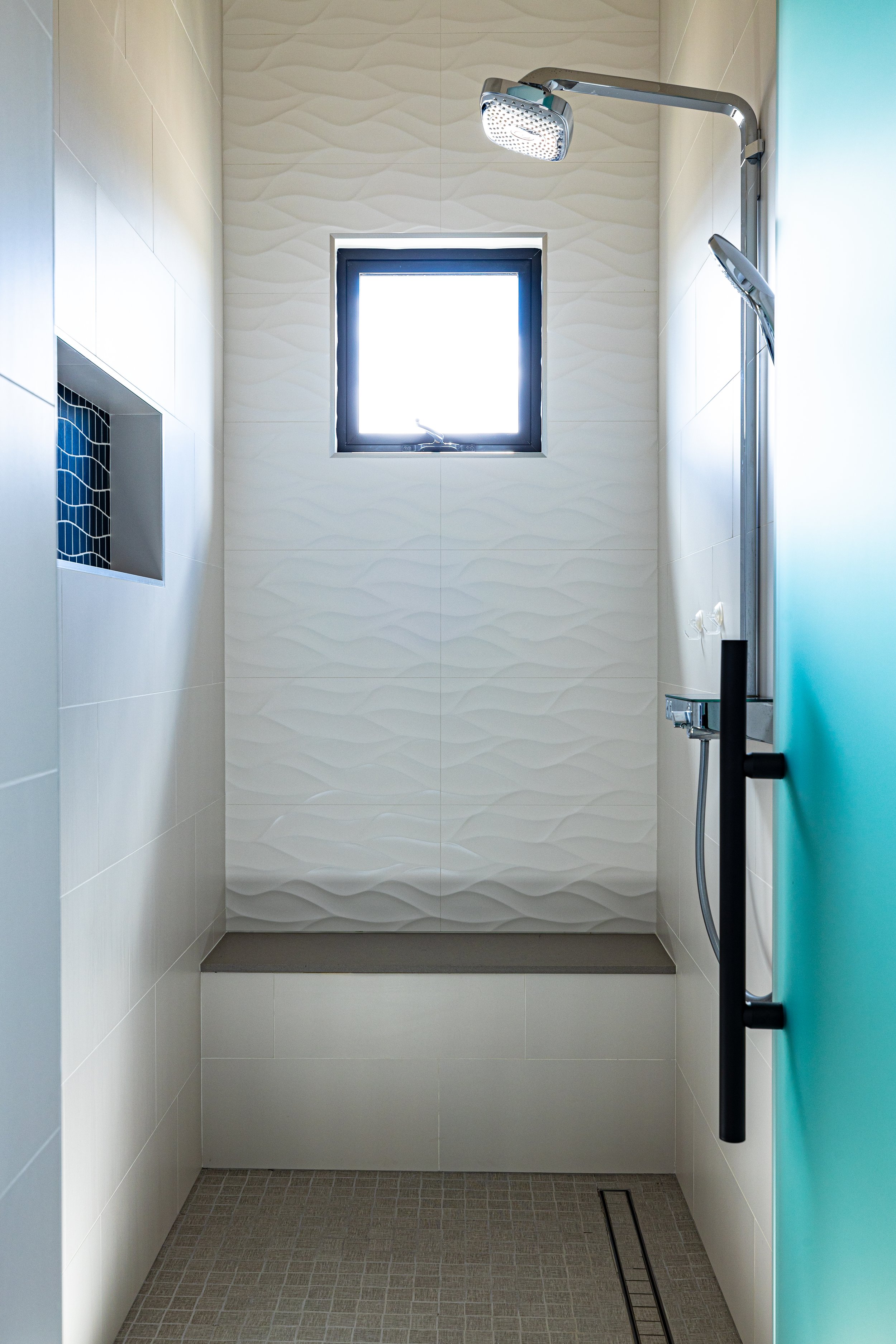 Modern shower with white tile walls, a small window, a rainfall showerhead, a handheld showerhead, and a teal door.