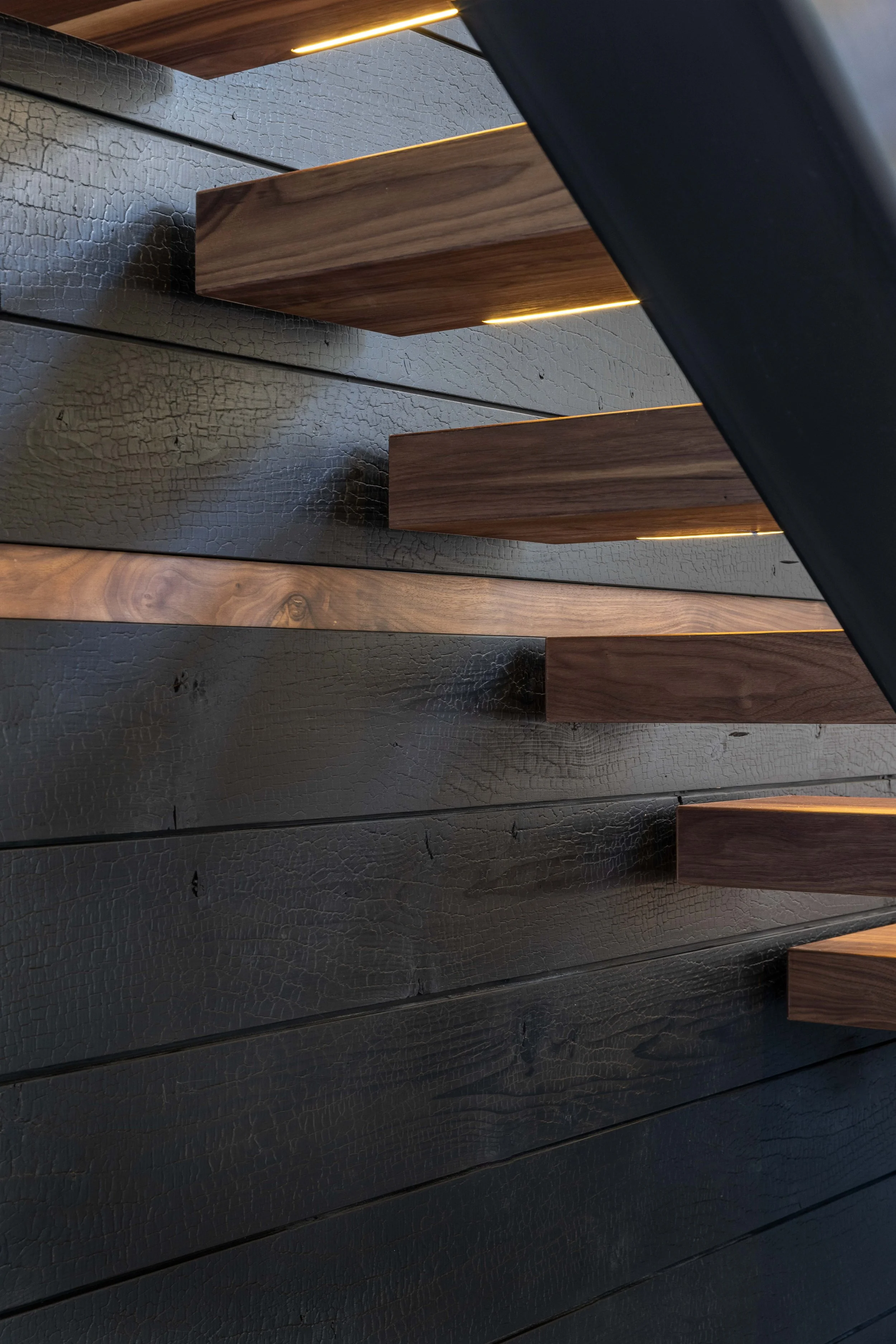 Close-up view of a modern walnut staircase with walnut treads and a Sugi ban and black walnut feature wall.