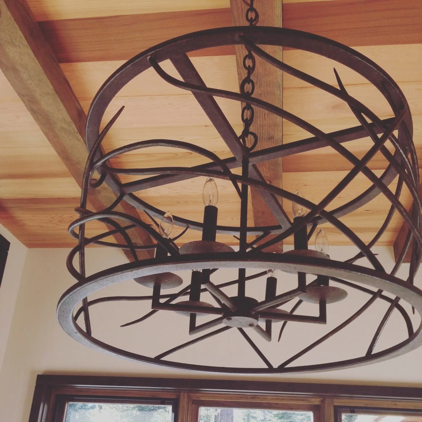 A custom designed black metal chandelier with branch inspiration with candle-shaped lights hanging from a chain. Designed by Emily Roose.