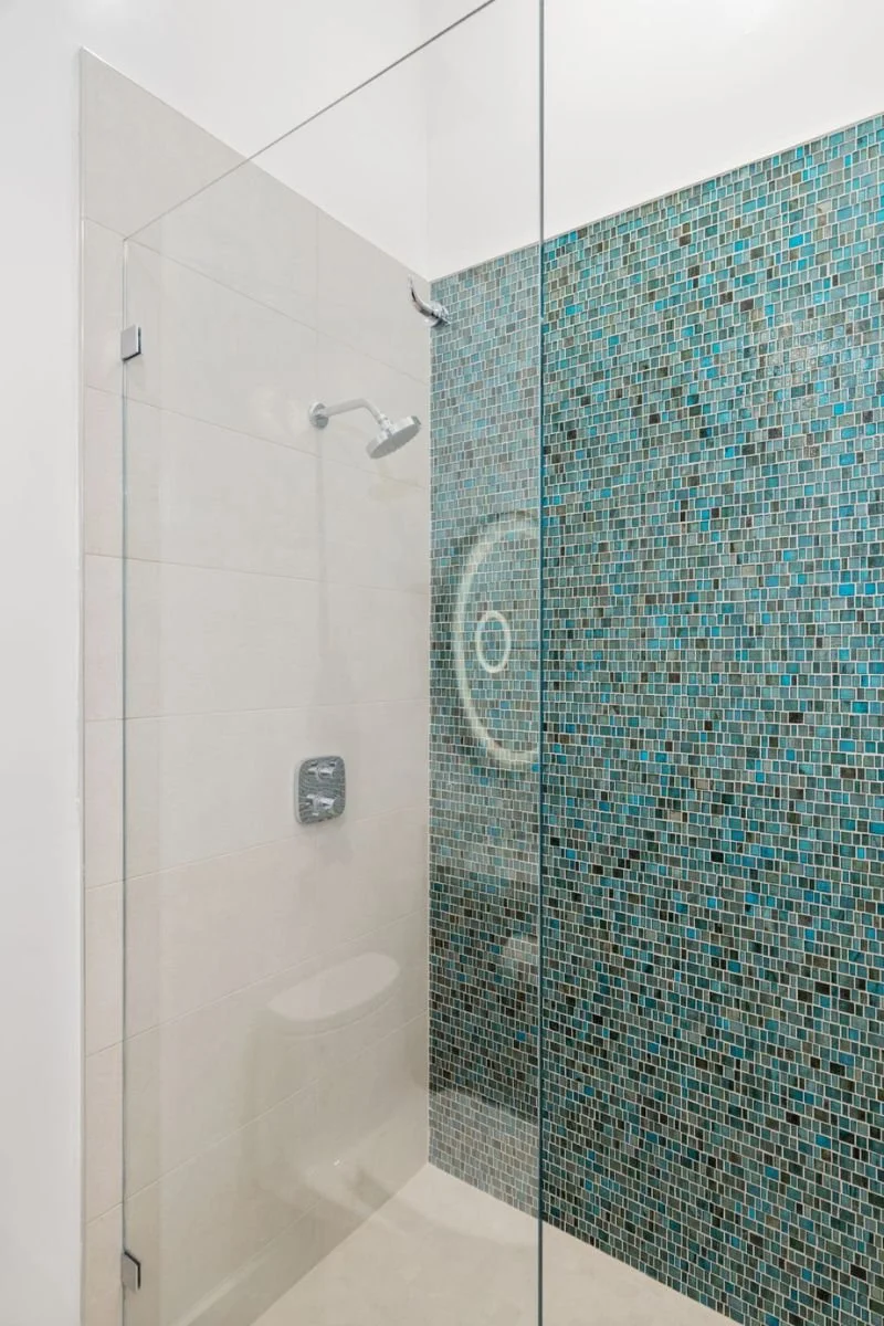 Shower area with tiled wall, glass door, showerhead, and control panel.