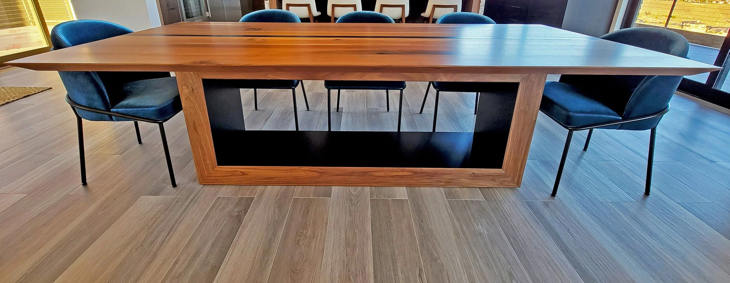 Large wooden conference table surrounded by black and blue chairs, with windows on the side letting in natural light.
