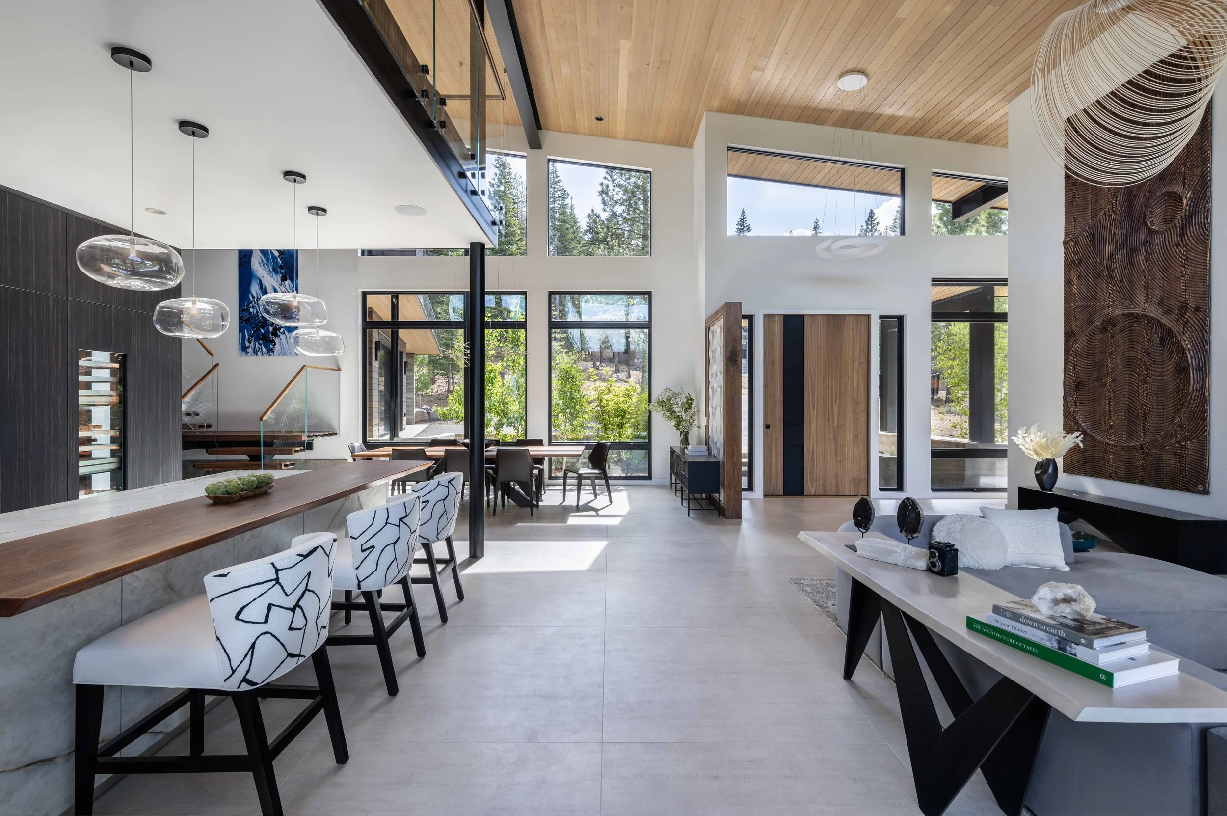 Modern open-concept living room and dining area with floor-to-ceiling windows, wooden accents, and contemporary furniture.