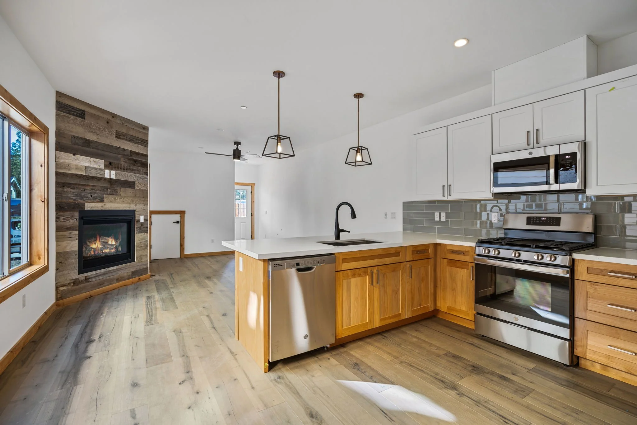 Modern kitchen with white cabinets, stainless steel appliances, and a wooden island with a black faucet, overlooking a living area with a fireplace and wood flooring.