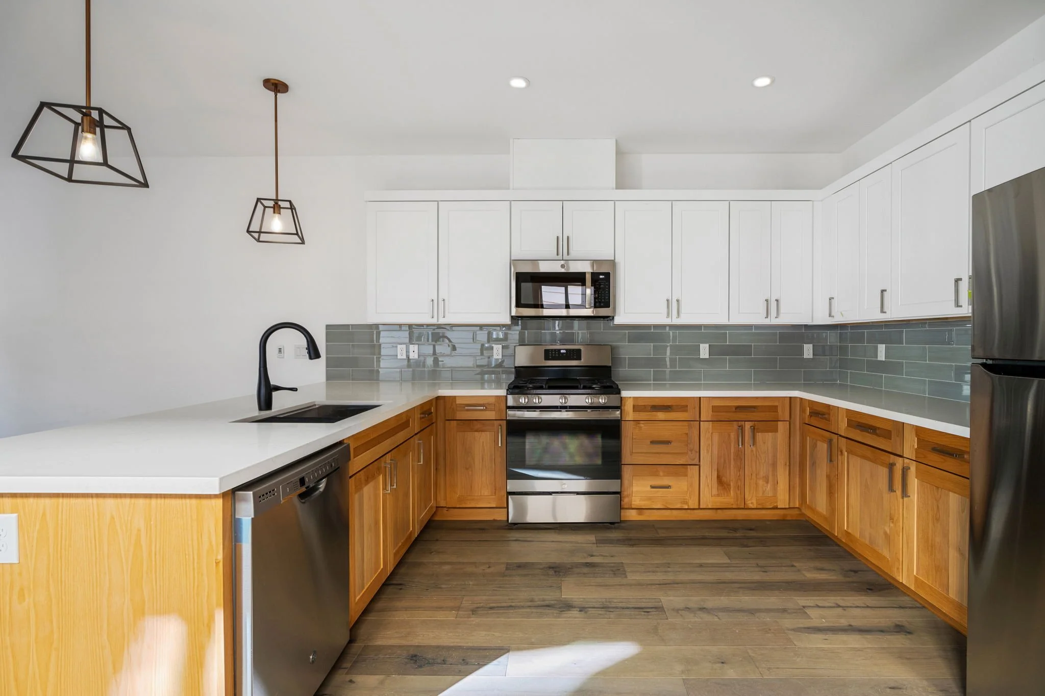 Modern kitchen with white upper cabinets, wooden lower cabinets, stainless steel appliances, gray tile backsplash, and wood flooring.