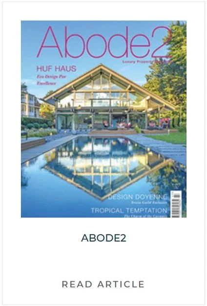 Magazine cover of Abode2 featuring a modern house with a large glass front, a pool reflecting the house, and lush greenery in the background.