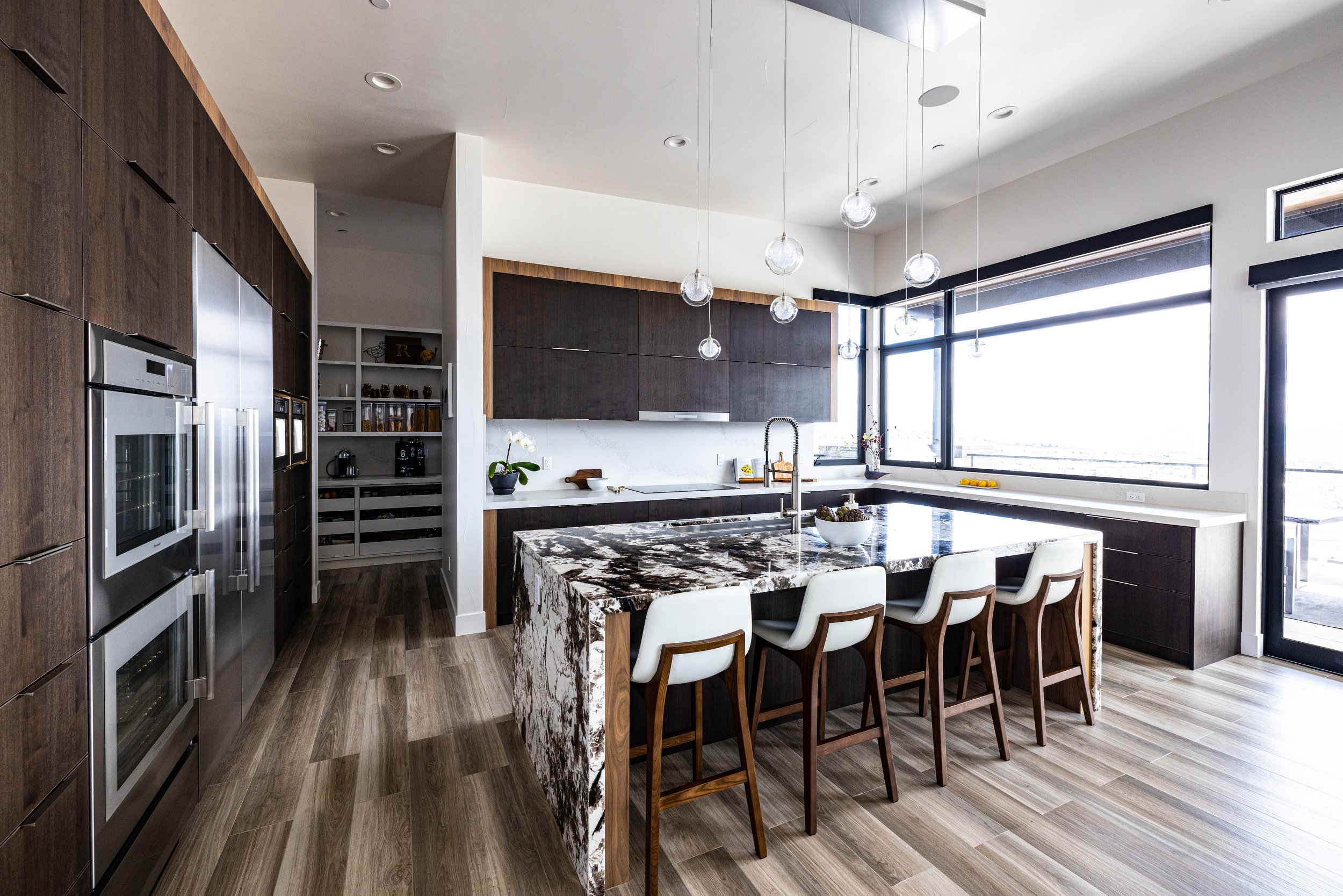 Modern kitchen with dark wood cabinets, a marble island with white and black patterns, a large window, and wooden flooring.