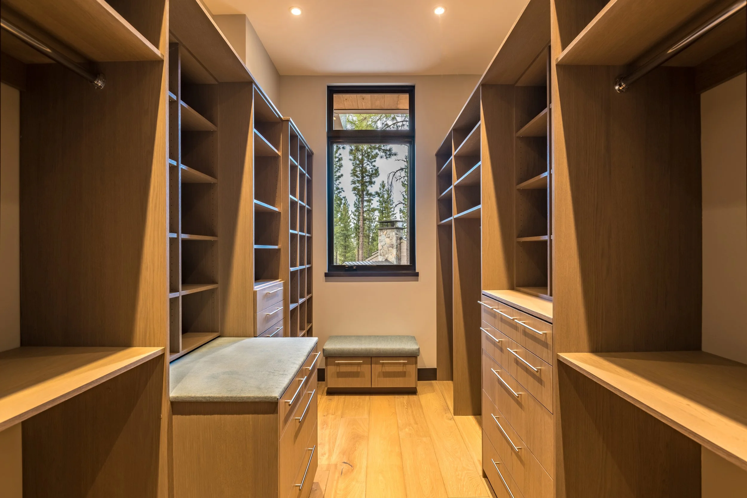 A walk-in closet with wooden shelves, drawers, and a window showing trees outside.