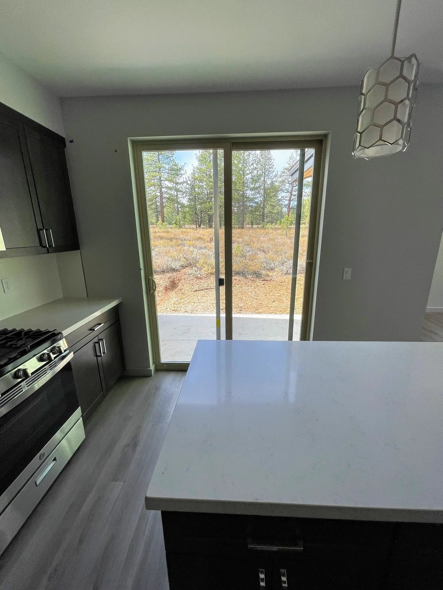 Kitchen area with gray cabinets, a stove, white countertop island, and sliding glass door leading to an outdoor patio with trees visible outside.