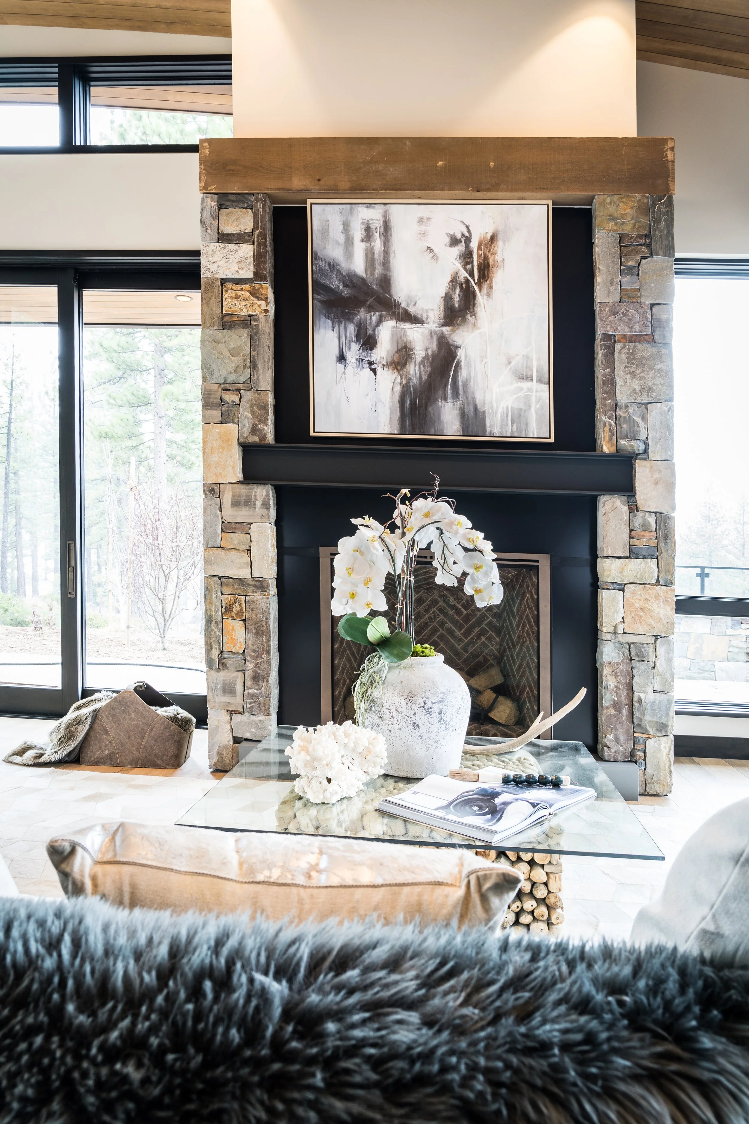 A living room with a stone fireplace, artwork above, and a glass coffee table with a large white orchid plant.