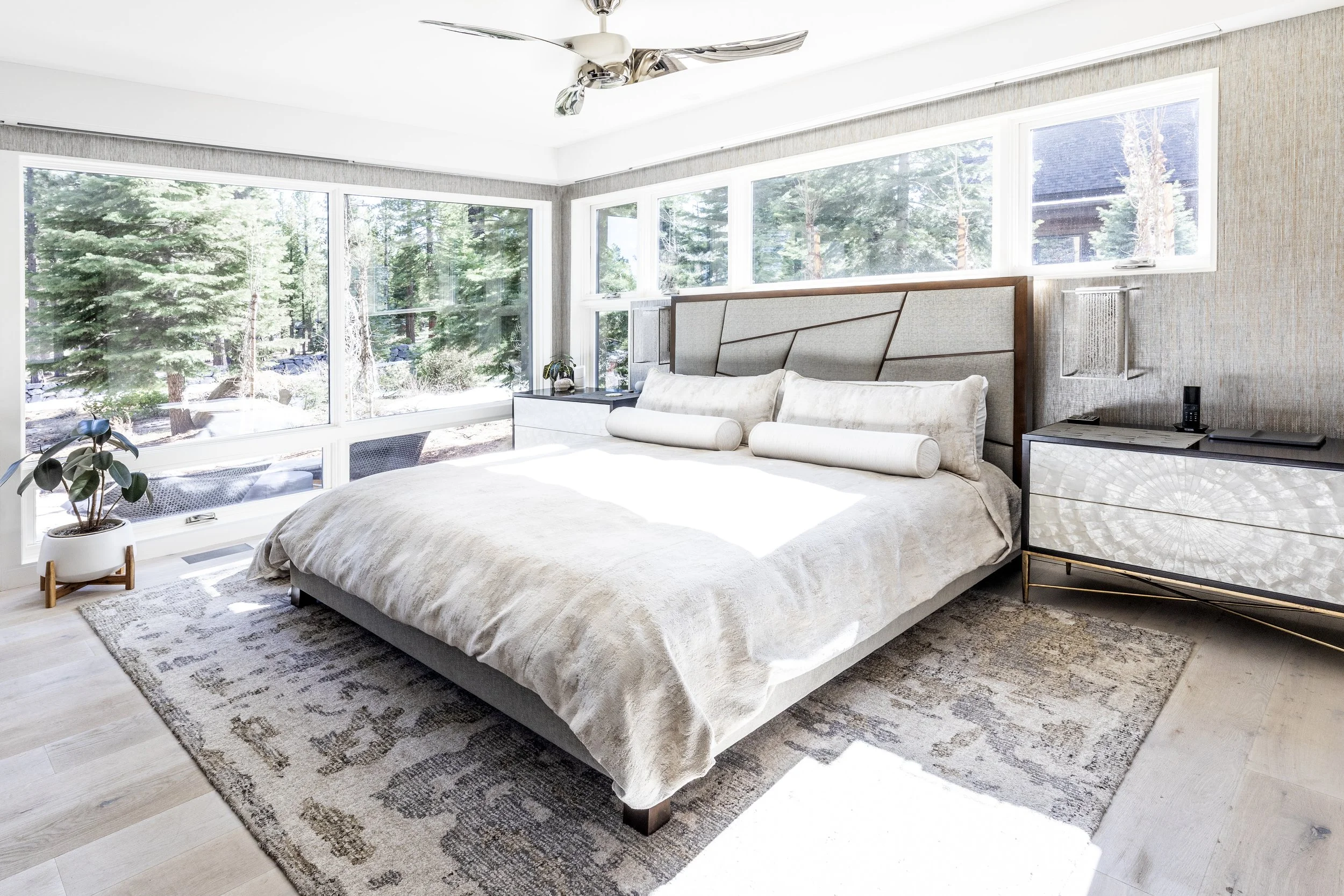 Primary mountain modern bedroom created to be luxurious with warm woods, cream, gold, and tan accents with the walls dressed in two different wallpapers. The window shades are recessed for a more modern and sleek design. Custom wood floors and ample 