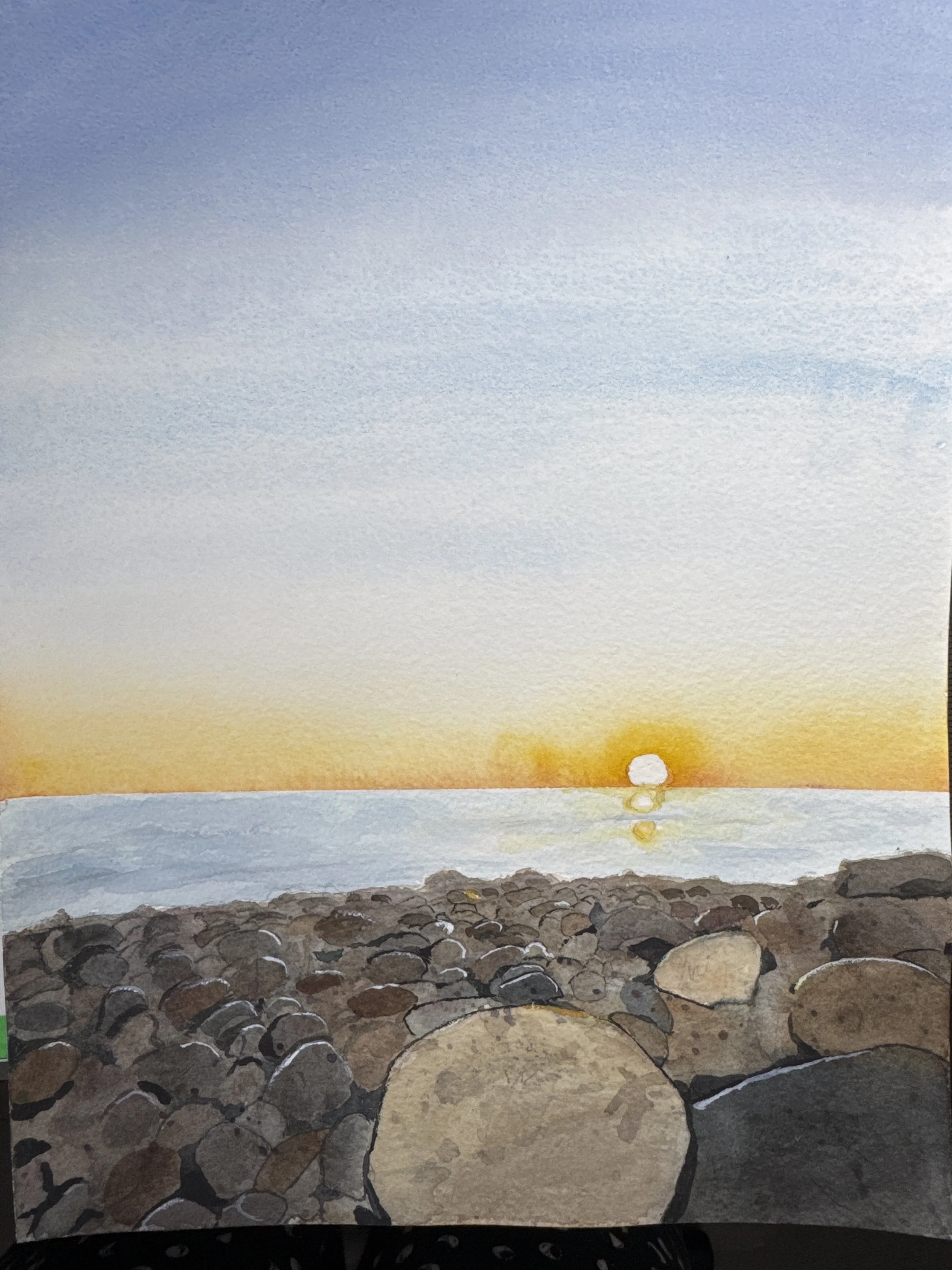 Painting of a sunset over a rocky shoreline with large stones in the foreground and a yellow-orange sun near the horizon.