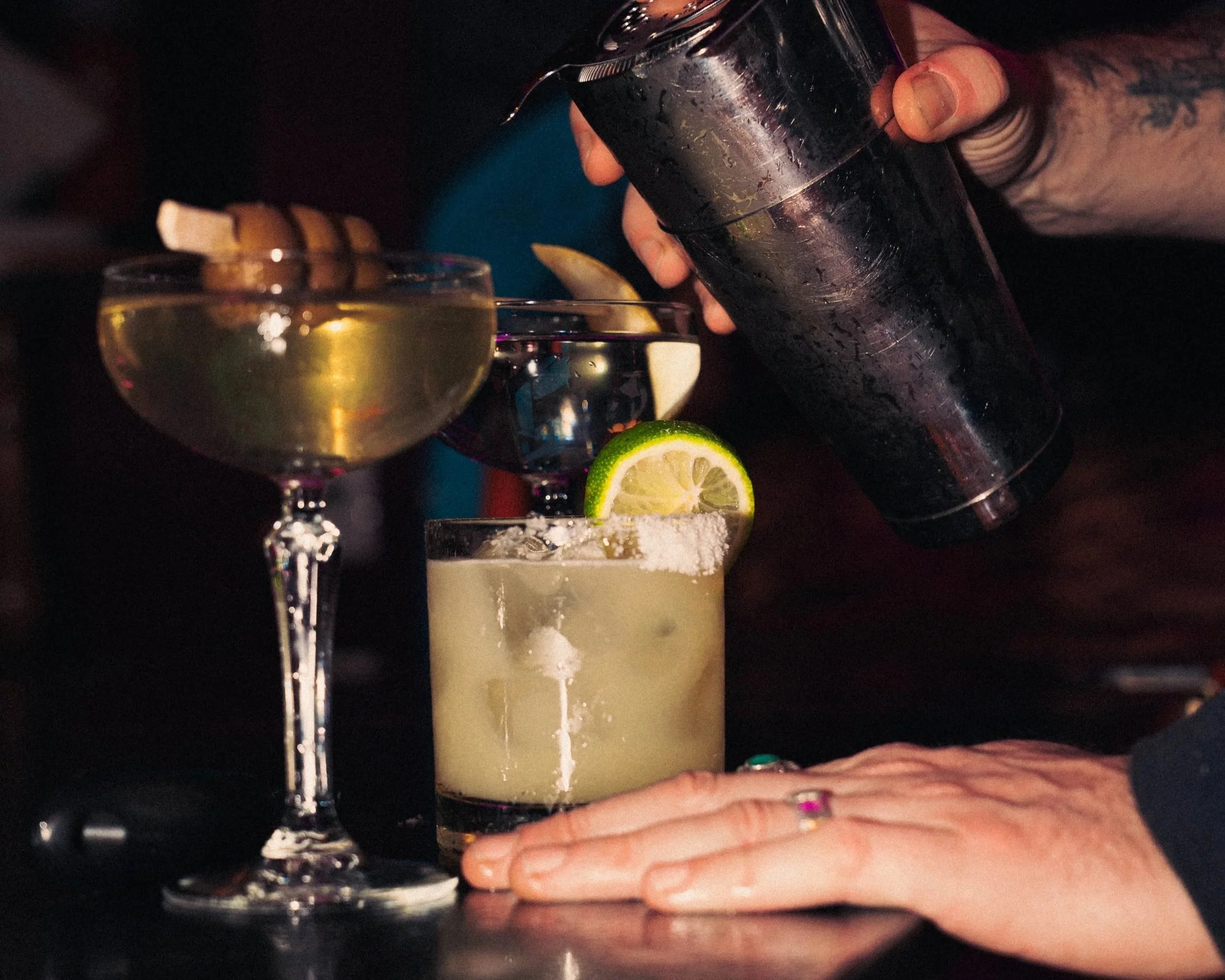 A bartender preparing a cocktail with lime, salt, and ice in a glass, while other cocktails with lemon slices and a garnished drink are on the bar counter.