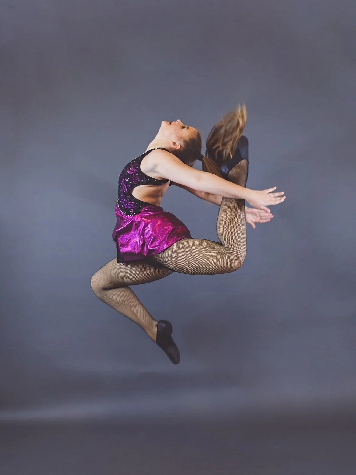 Kayla performs a leap against a gray background.