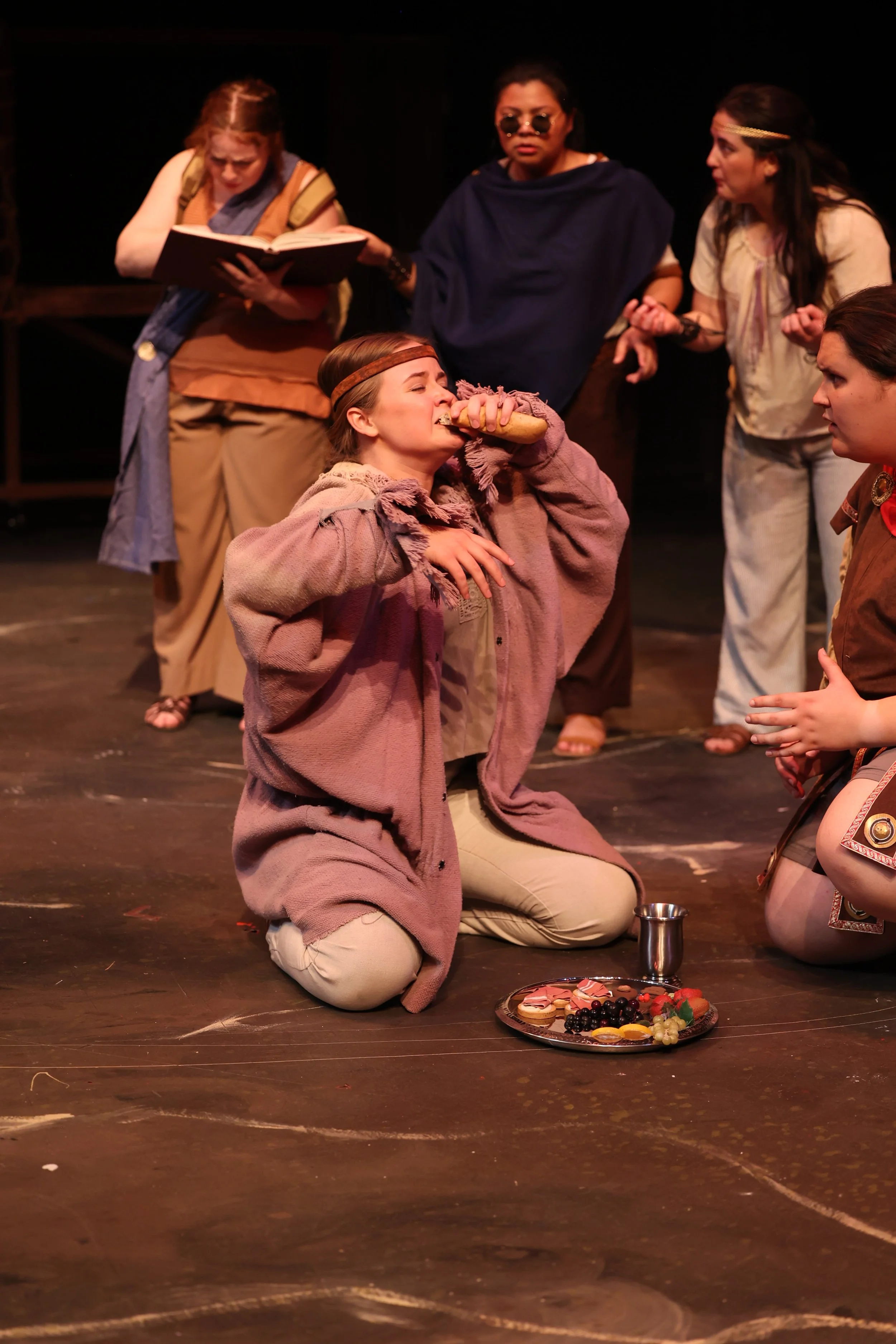 Kayla in Argonautika by Mary Zimmerman, portraying the character Phineus, kneeling and eating food from a plate on the floor. 