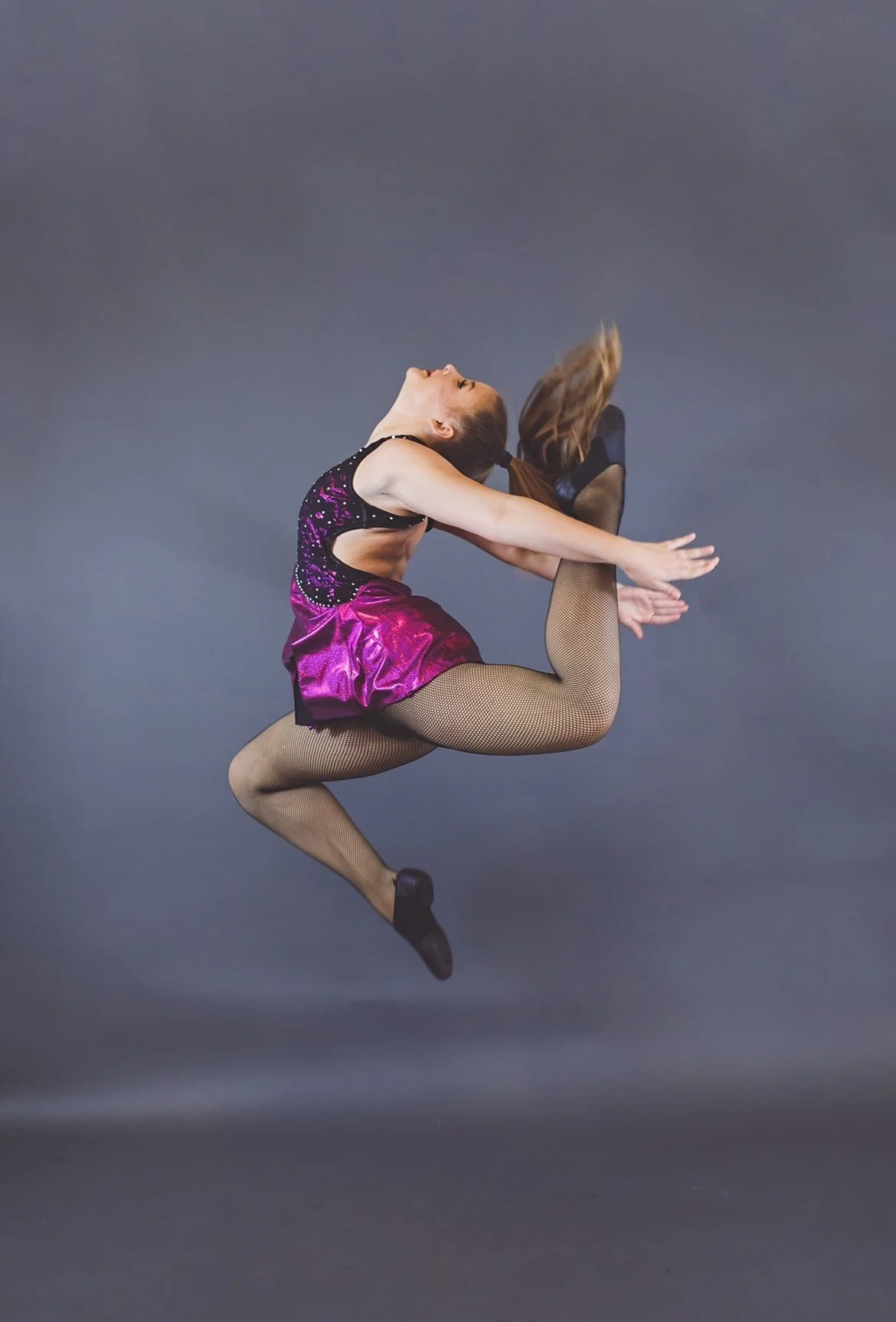 Kayla performs a leap against a gray background.