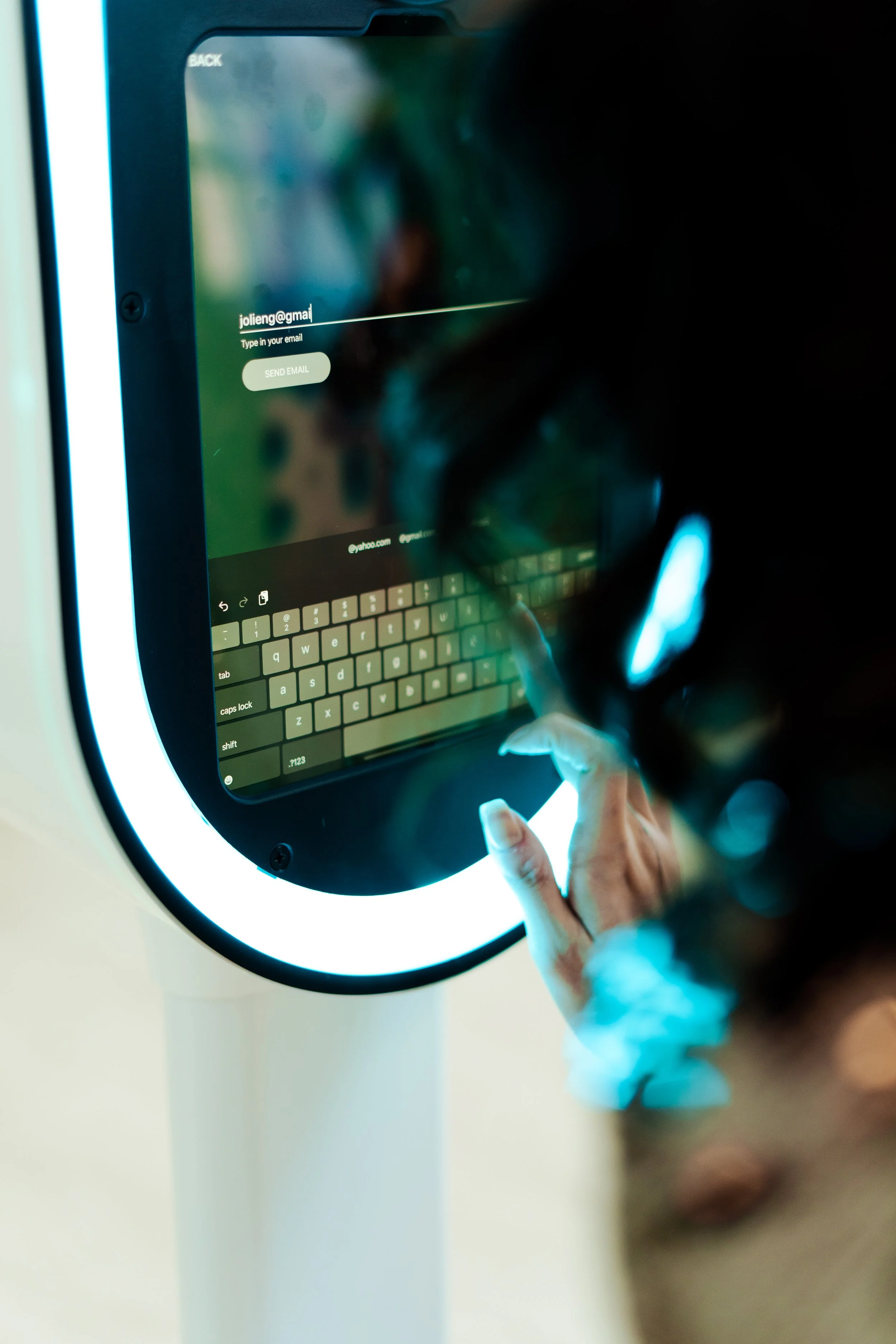 Person using a touchscreen Photo Booth kiosk to input an email address, with a keyboard visible on the screen.