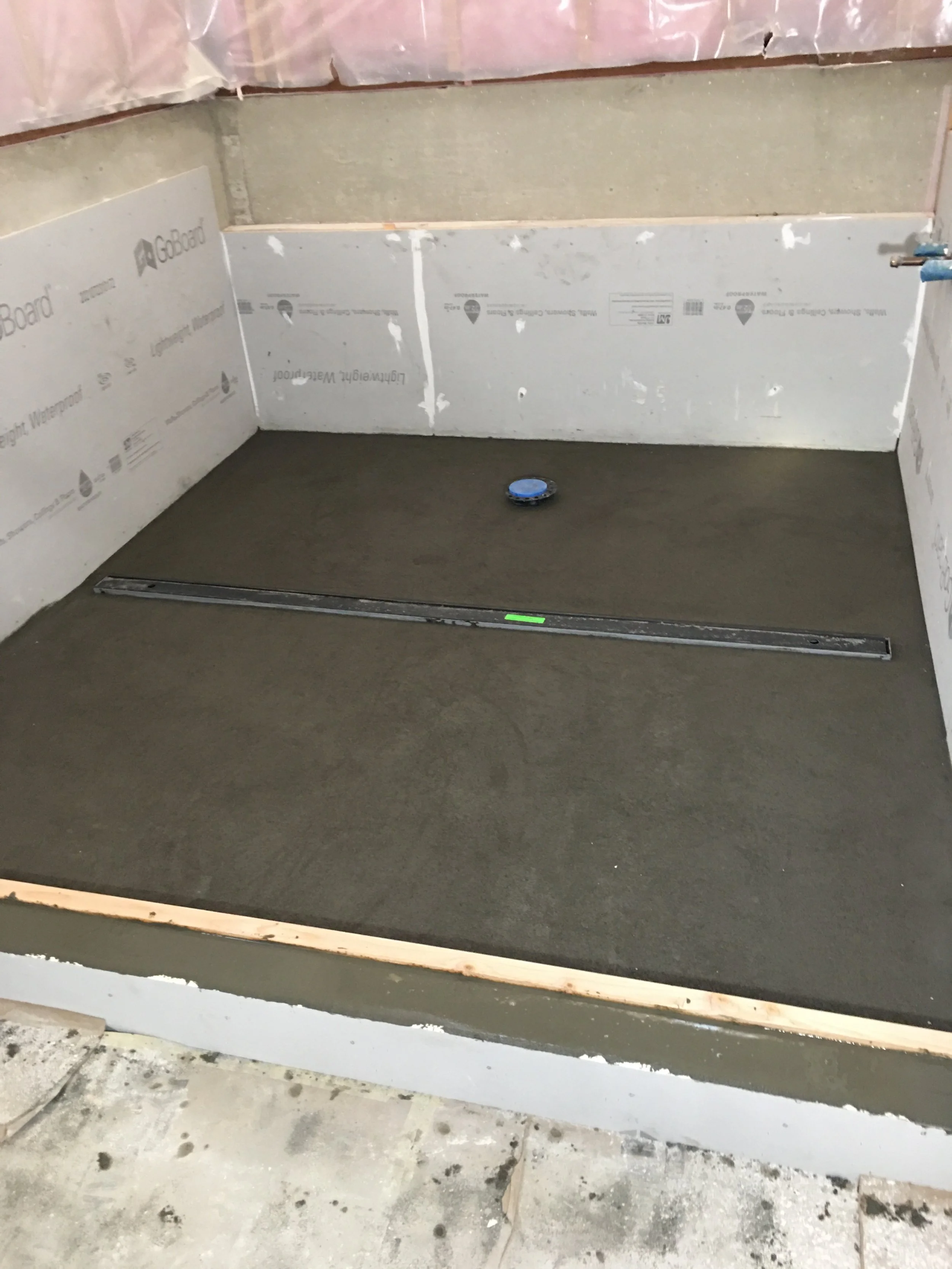 Construction site showing a partially installed shower base and unfinished walls with insulation and waterproofing layers.
