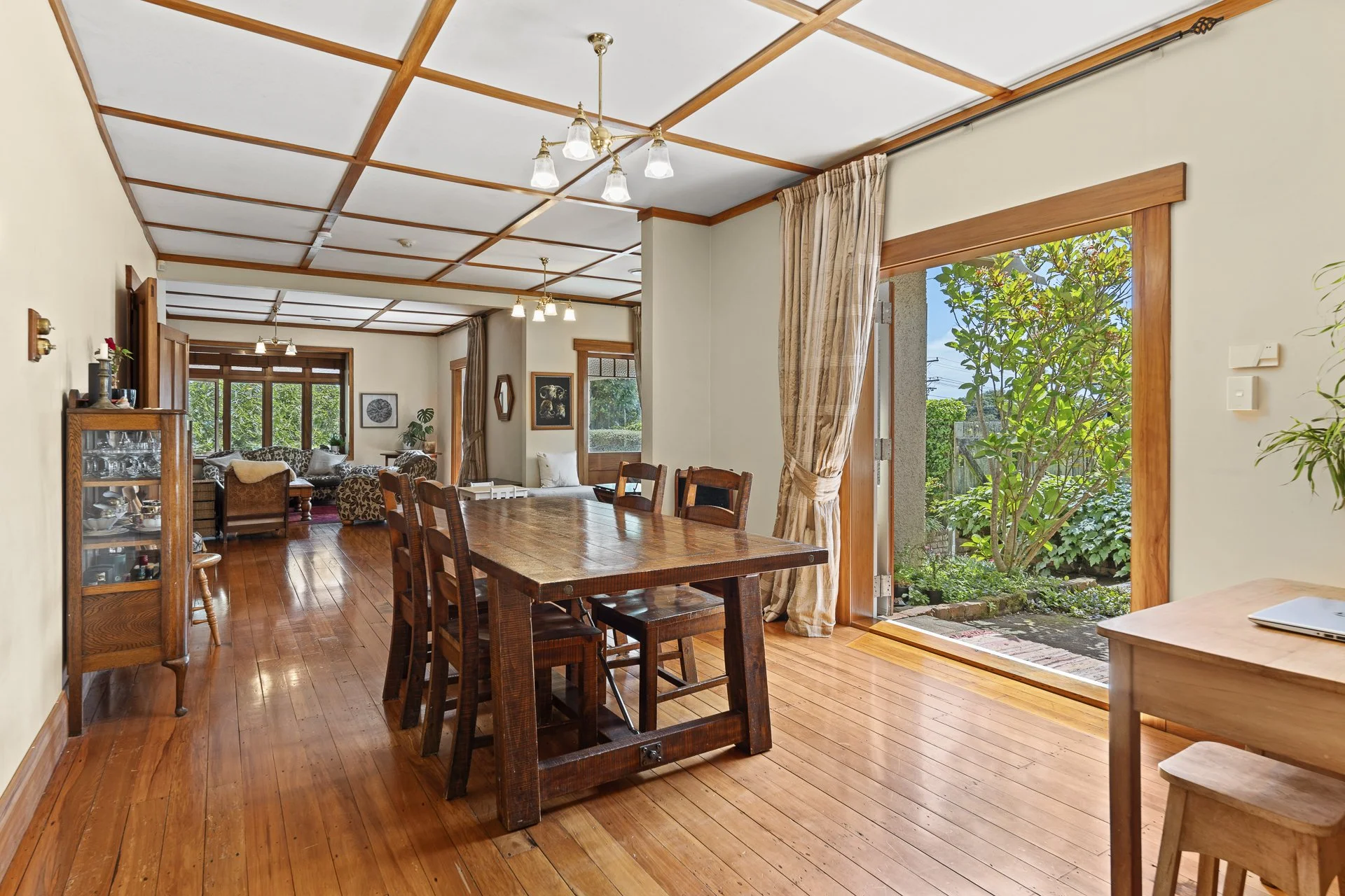 Rimu Street, New Plymouth.  Character home with  a dining area with wooden floors, and large windows with curtains that open to a garden with green plants and trees.