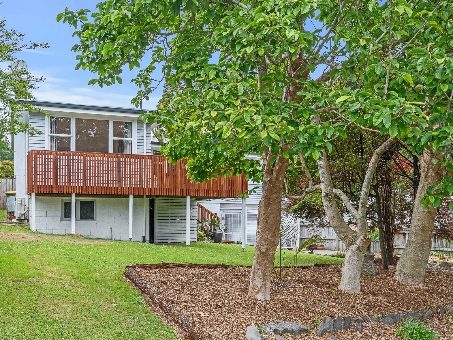 174 Huatoki Street, Vogeltown, New Plymouth.  A backyard with green grass, trees, and a house in the background featuring a wooden deck and large windows.