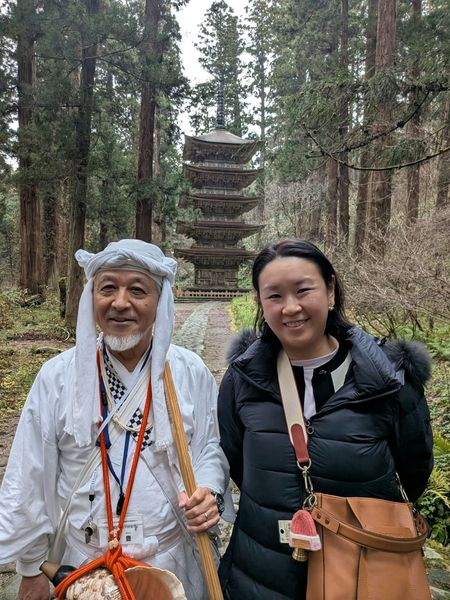 TokudAw's CEO standing in front of a pagoda in the forest with a monk specialized in mountain practice wearing white