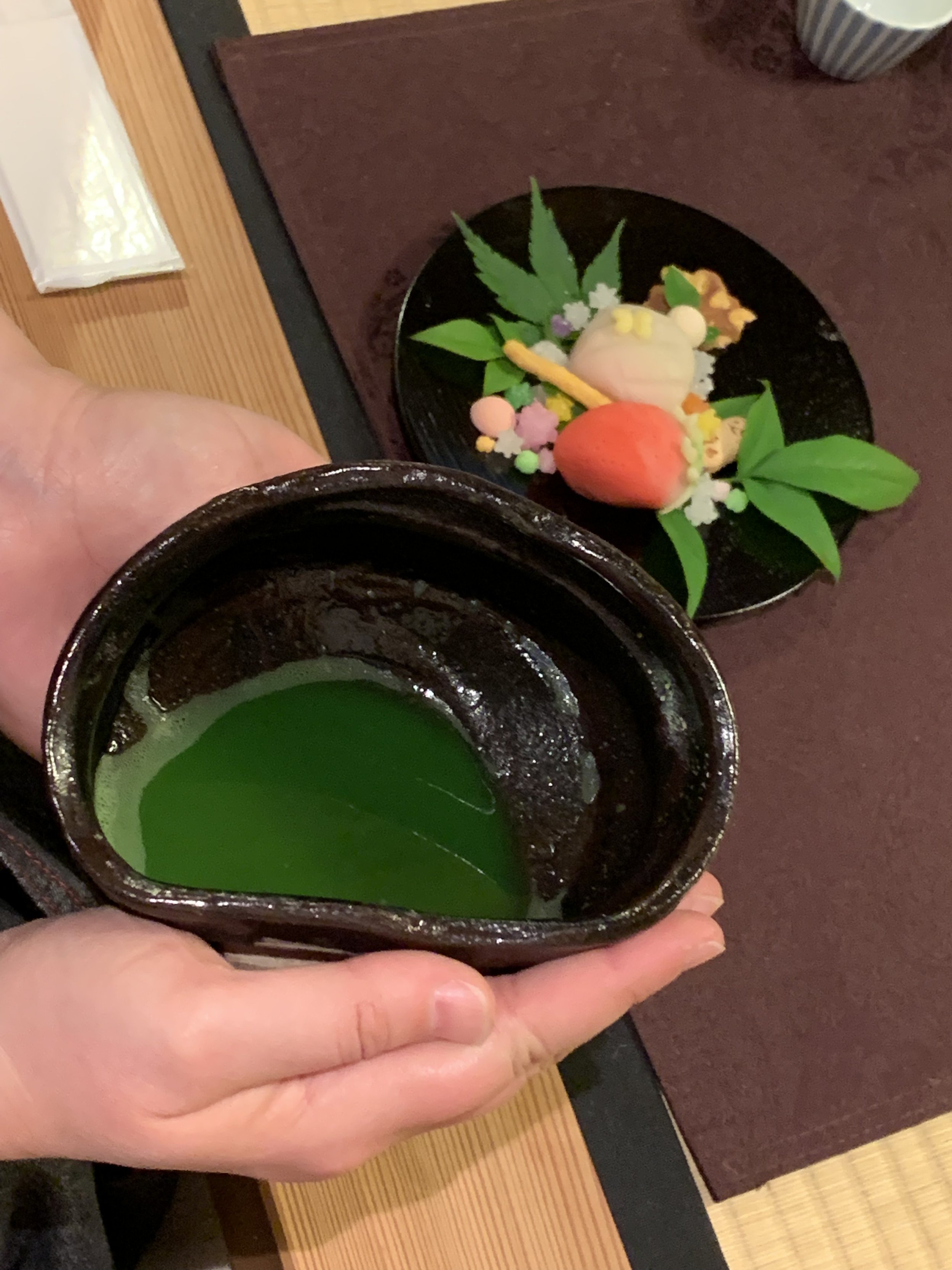 Two hands hold a ceramic tea bowl that contains matcha and that is irregularly shape