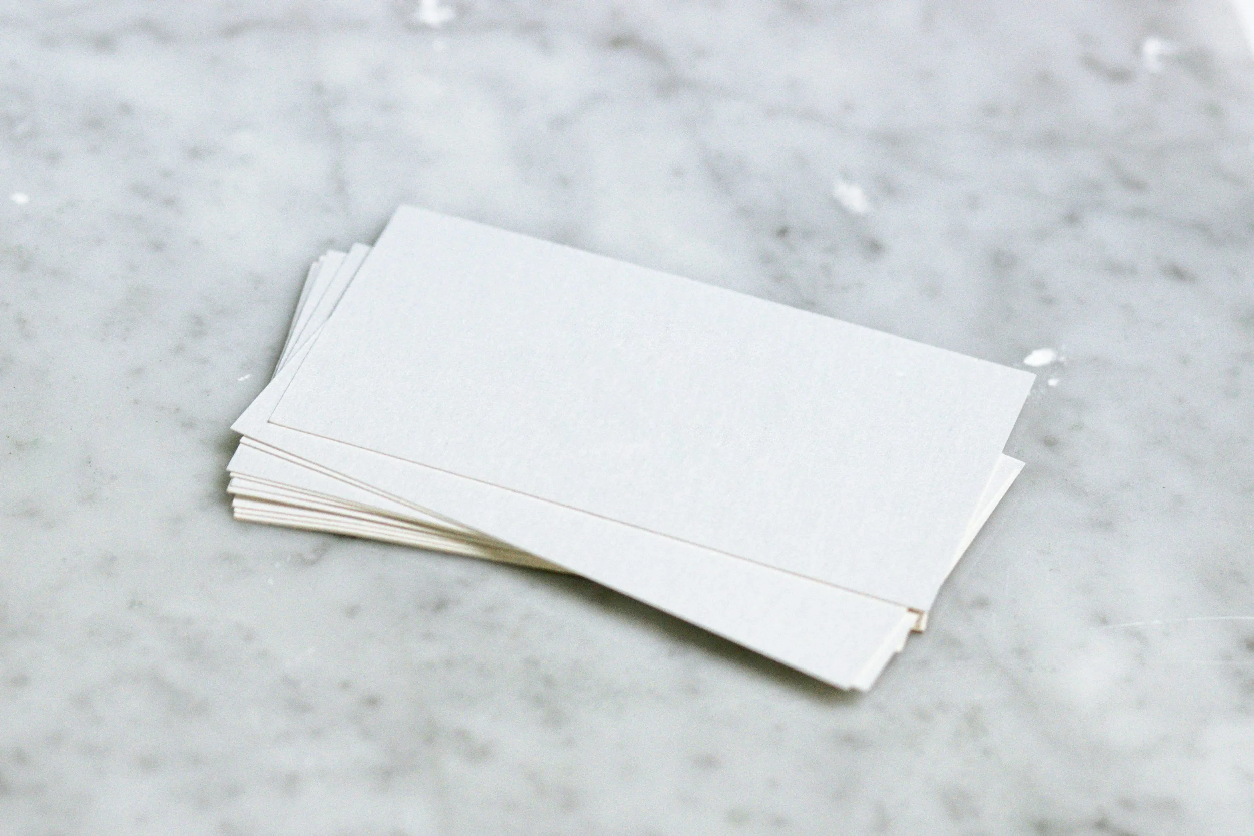 A stack of white business cards sits in a slightly messy stack on a gray and white granite countertop.