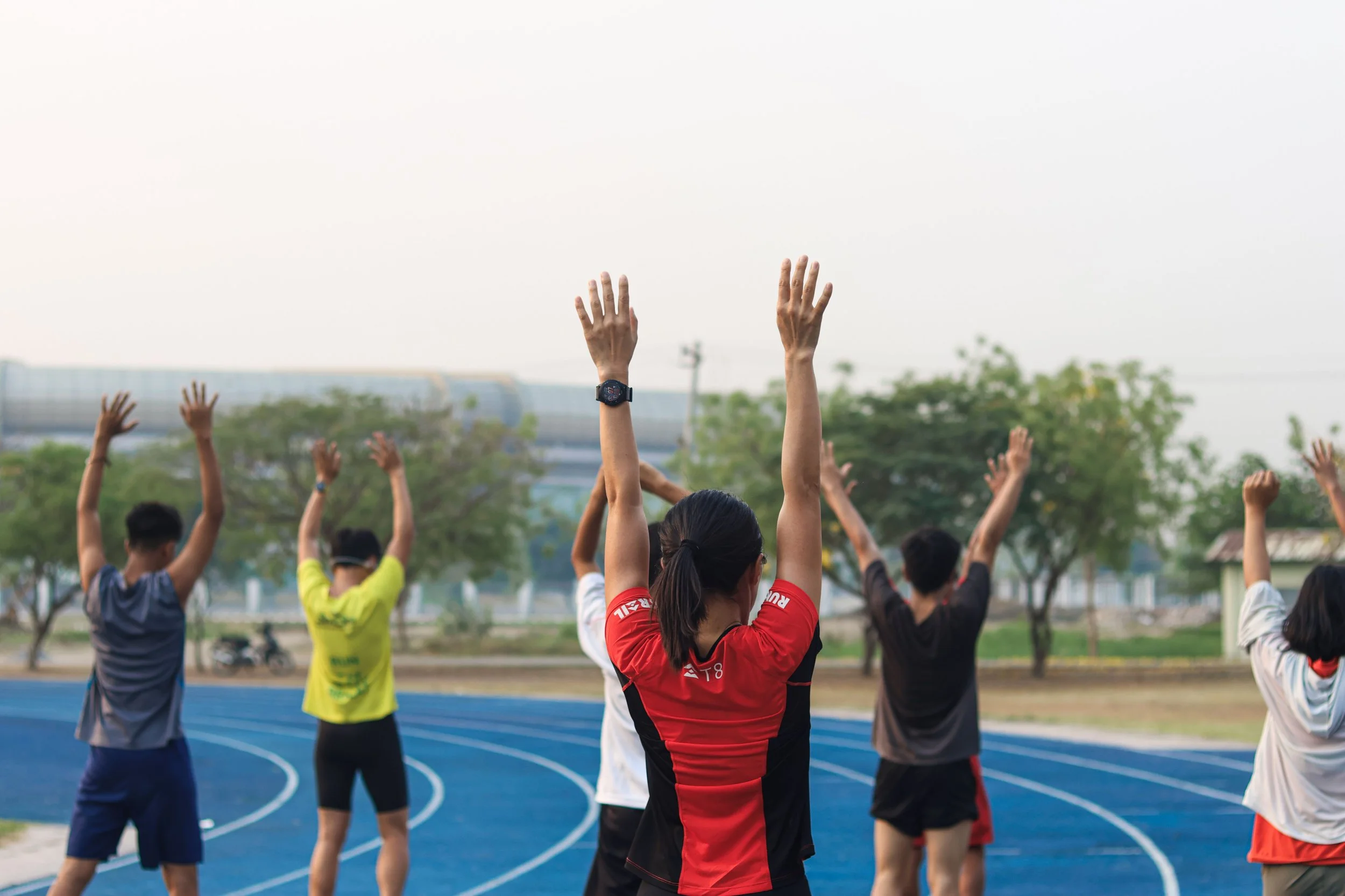 A group of people dressed in athletic clothes are warming up together on a trackfield