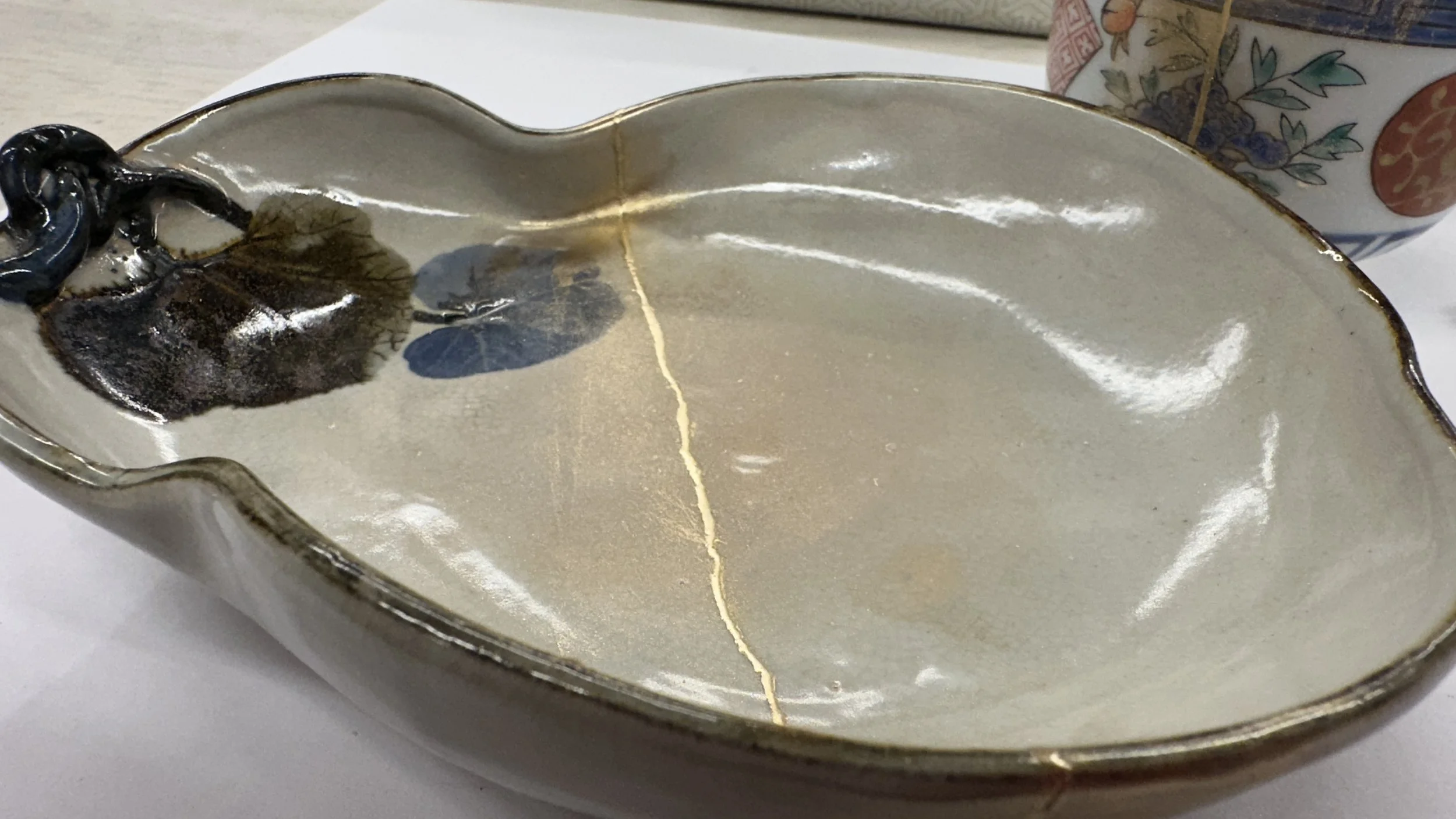 A ceramic plate with a golden crack in the middle and a cup that has been repaired with gold
