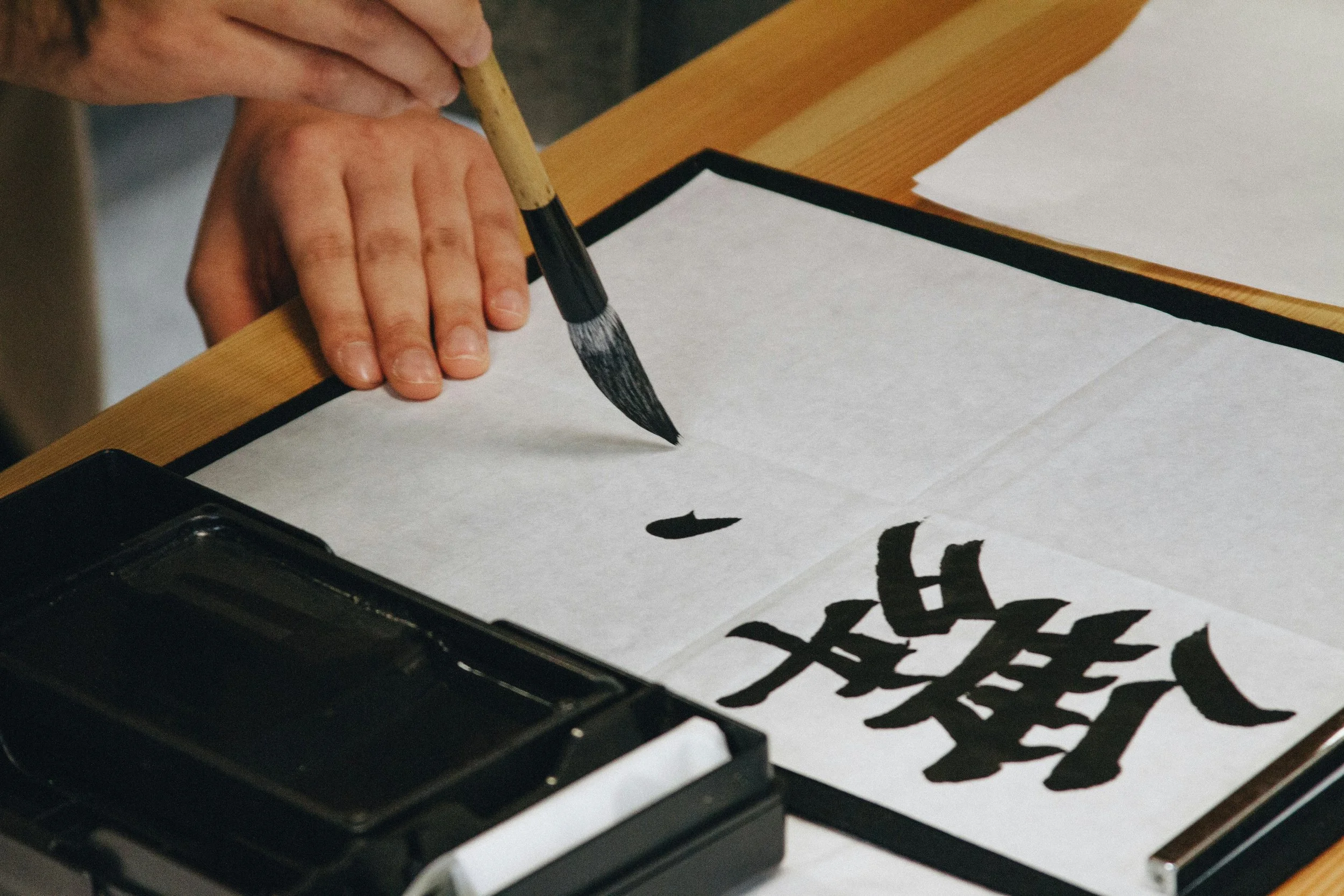 A hand is holding a special calligraphy brush and is writing with ink on a piece of paper