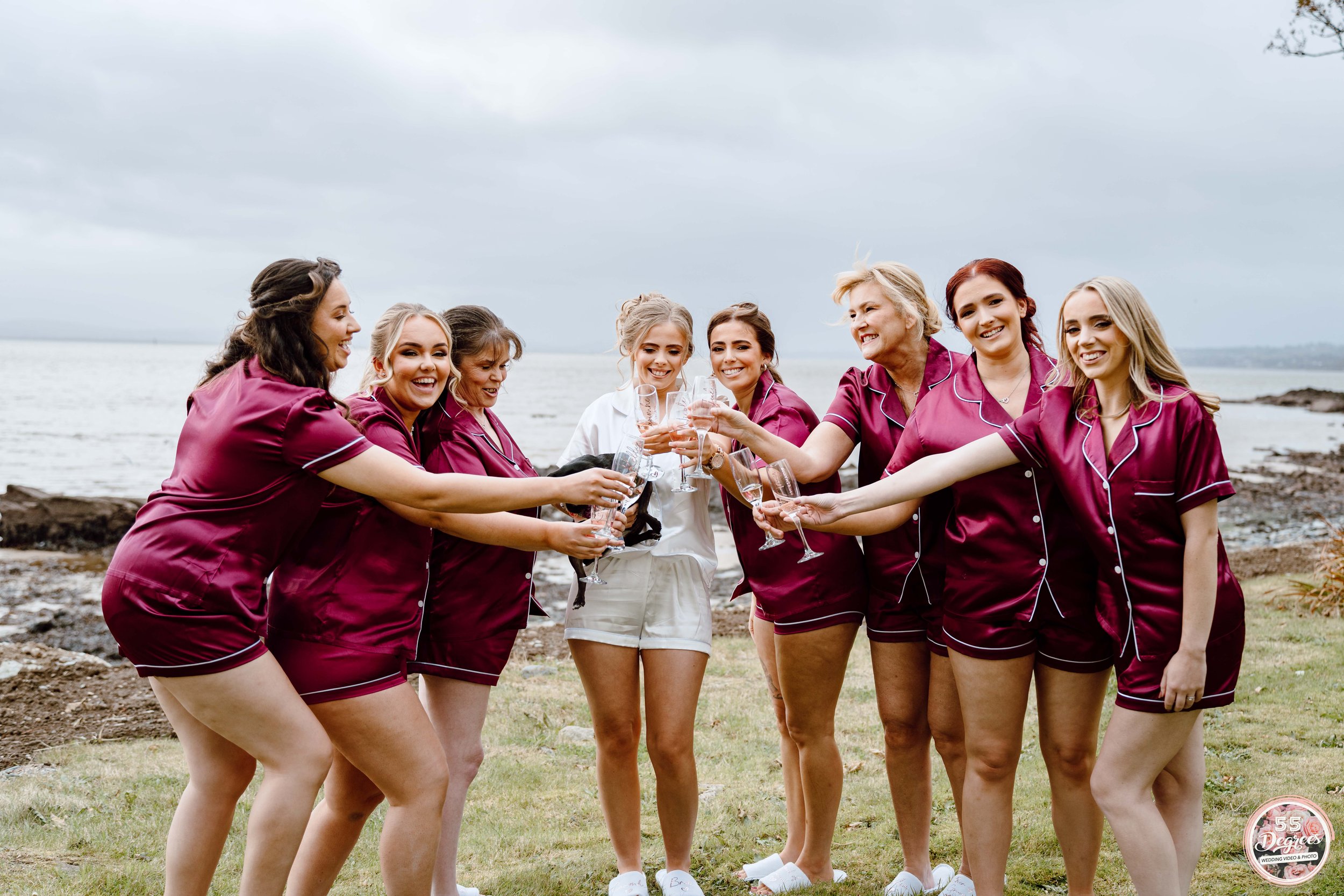 Group of women in matching maroon pajamas celebrating with champagne at the beach