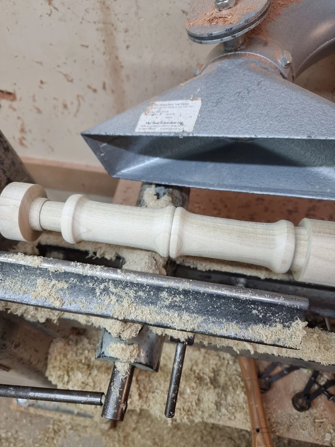 A woodworking router with a wooden table leg being carved, surrounded by sawdust and wood shavings.