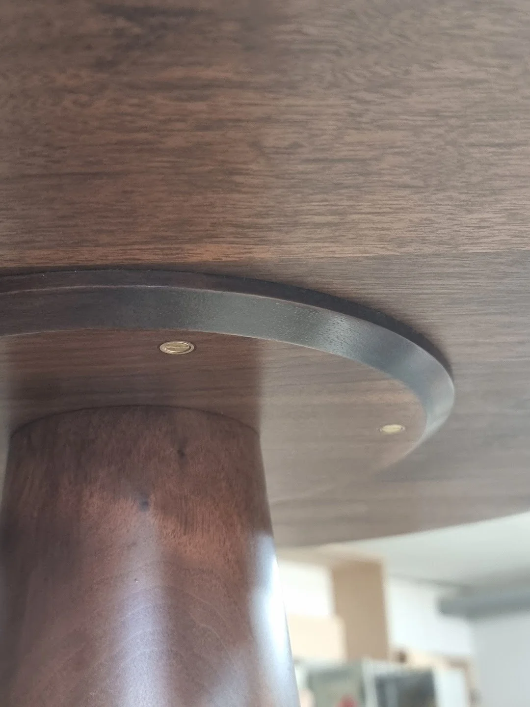 Close-up of a wooden table's underside showing a round support with screws and a wooden leg.